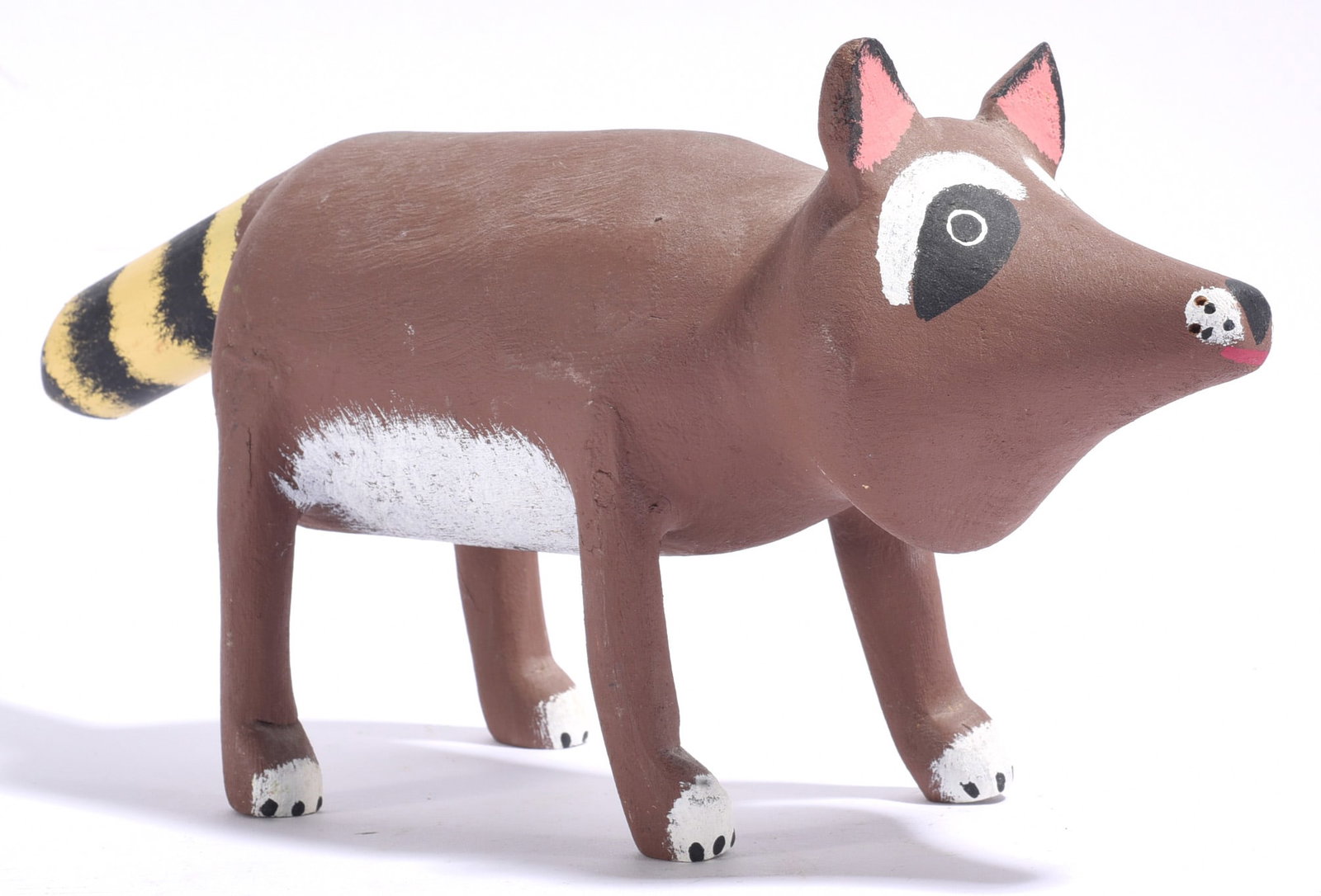 David Alvarez Folk Art Carving: 13"x6" David Alvarez folk art carving of a raccoon, hand carved and painted with a brown body, striped tail, white feet and boldly outlined facial markings. A charming example of contemporary animal-o