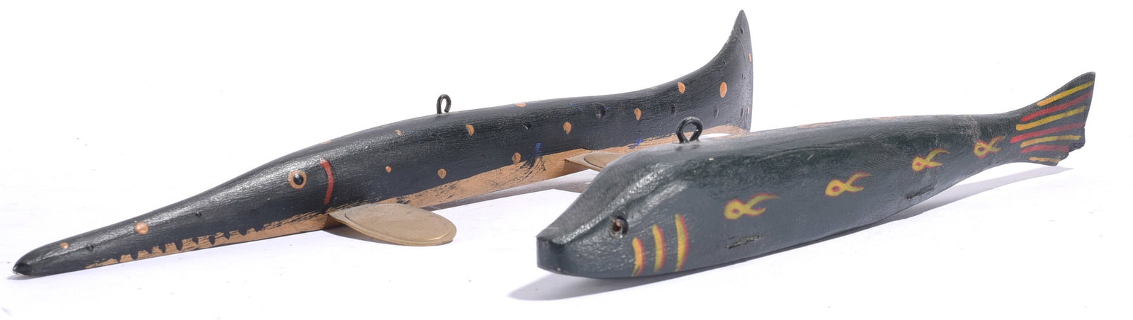 Vintage Carved Fish Decoys (2): Largest is 11.5"x1" Pair of carved and painted wooden fish decoys in dark tones, one long slender example with copper-colored accents and one broader fish decorated with small yellow and red fish
