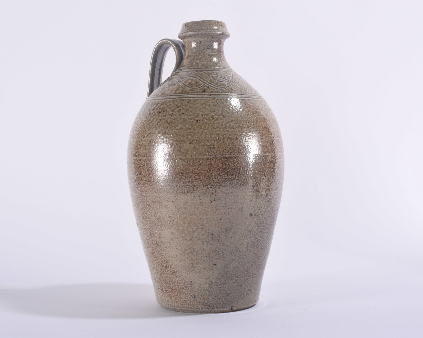 Travis Owen Jugtown Pottery Jug: 11" Travis Owen Jugtown pottery jug with tall ovoid body, single applied handle and incised looping decoration around the shoulder. Finished in a warm gray-brown glaze with natural firing variation.