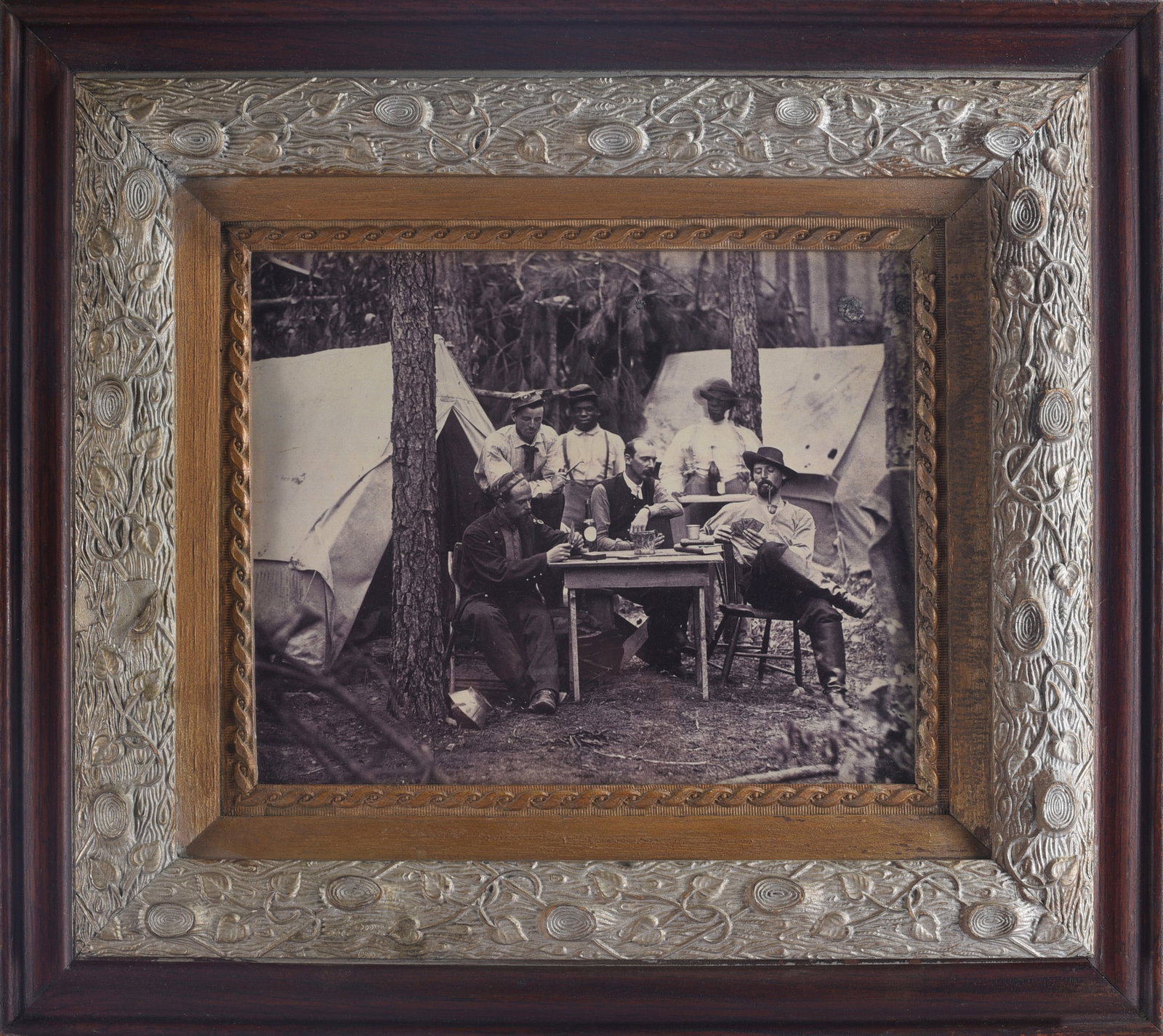 Black and White Photo of Soilders in Camp: 21"x19" Black-and-white photograph depicting a group of men gathered around a table at a wooded campsite with canvas tents in the background, presented in an ornate period-style frame.