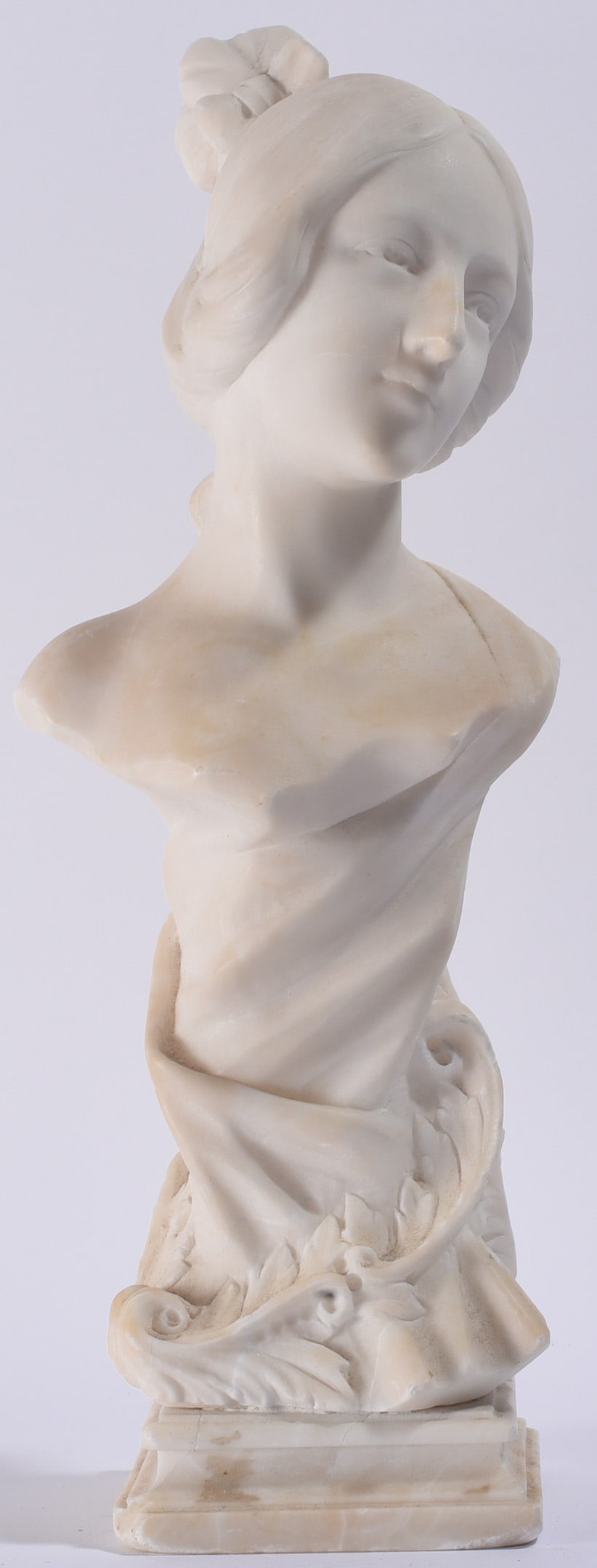 Carved Allibaster or Marble Bust: 15" Carved alabaster or marble bust of a young woman with upswept hair and classical drapery, raised on an integral decorated base.