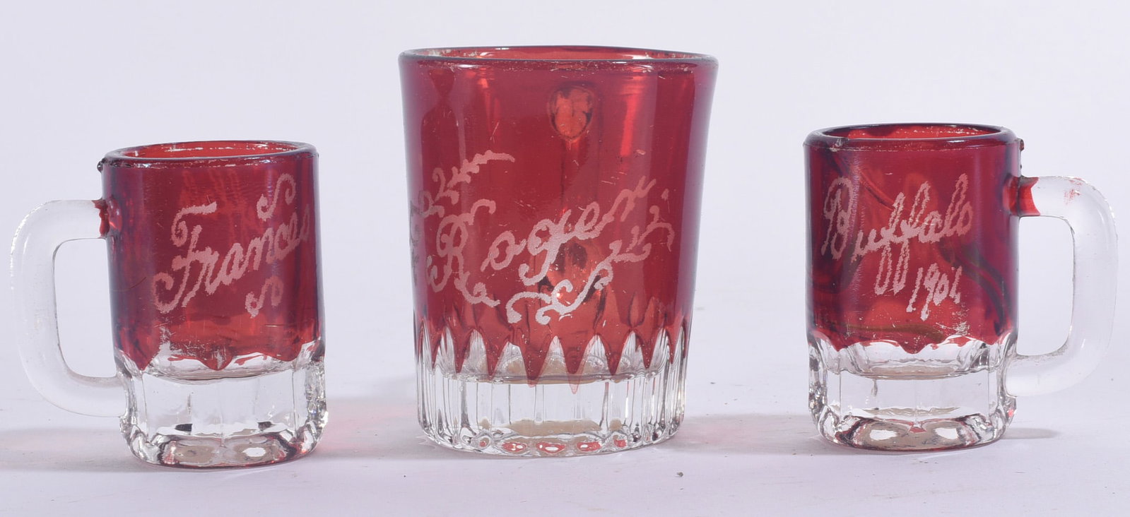 Ruby Cut to Clear Glass Cups: Largest is 2.5" Group of three ruby cut-to-clear glass drinking vessels including two handled cups and one tumbler, each with engraved decoration.