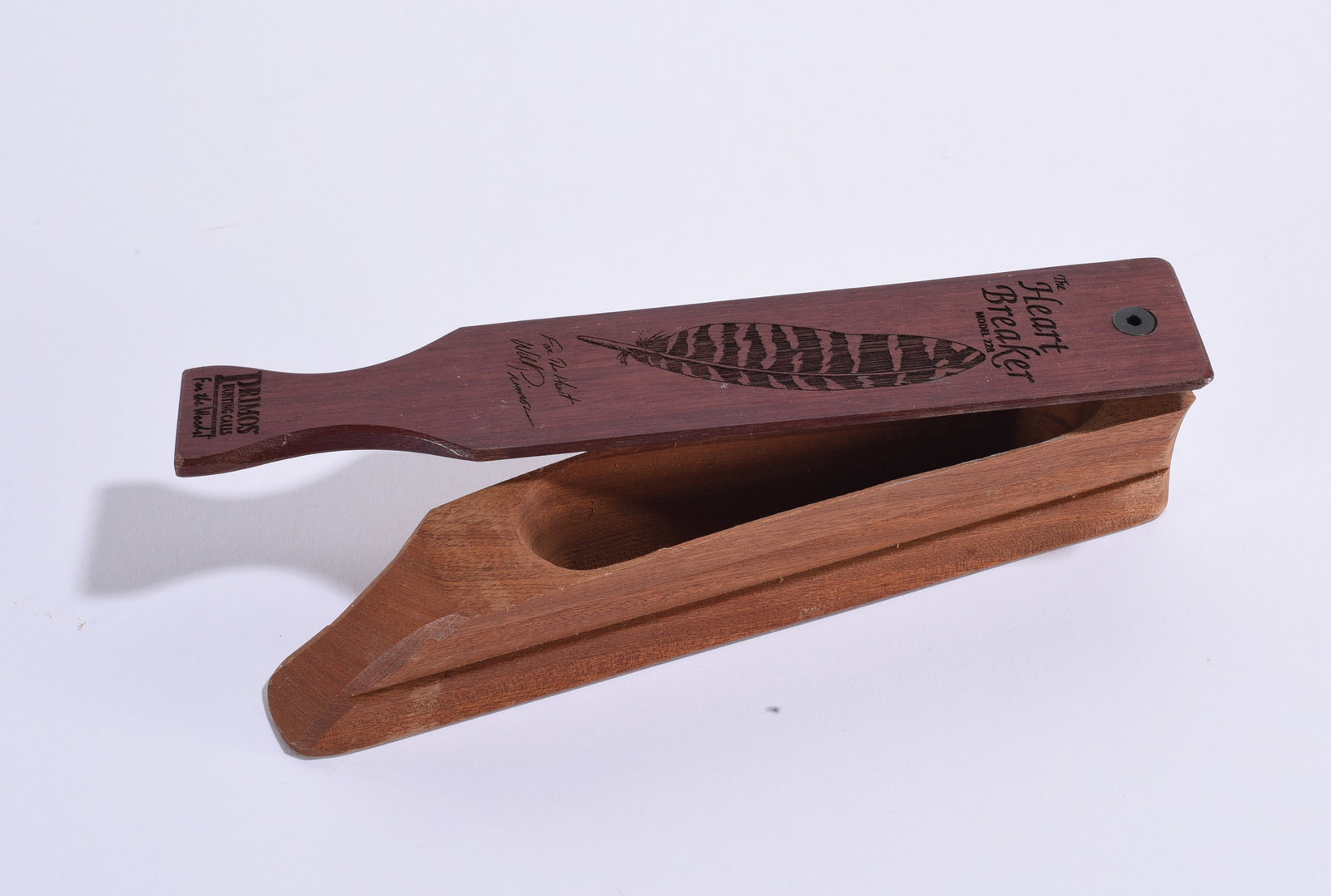 The Heart Breaker Model 228 Turkey Box Call by Primos: 9"x2" Primos "The Heart Breaker," Model 228, wooden turkey box call. Reddish hardwood paddle is marked with feather graphic, "The Heart Breaker Model 228," Primos Hunting Calls and Will Primos marking