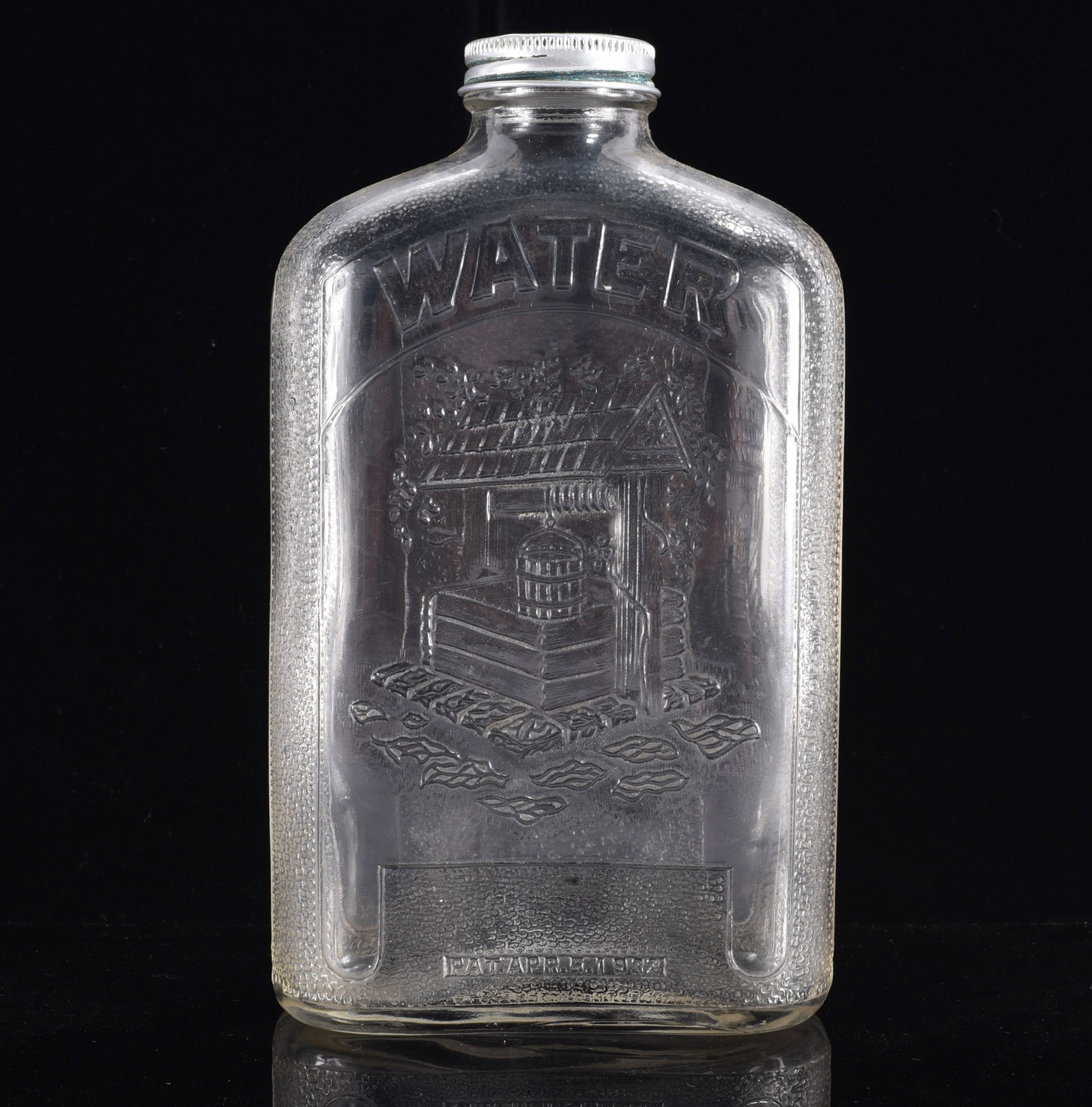 Antique Embossed Water Bottle with Screw Cap: 9" Vintage clear glass water bottle of flattened rectangular flask form with screw cap, boldly embossed "WATER" above a detailed image of an old-fashioned covered water well. Textured border surrounds