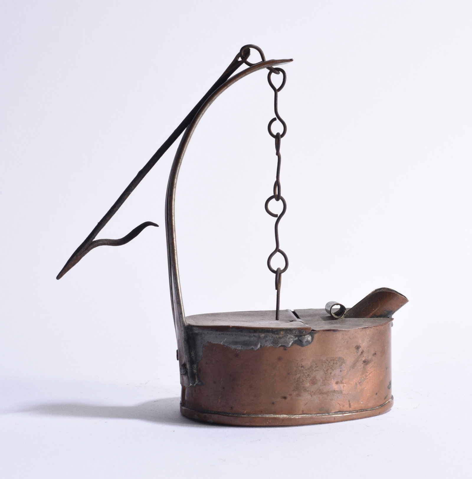 Early American Lighting: Early American primitive lighting device constructed of copper and wrought iron, having an oval copper reservoir with hinged top, projecting curved iron standard and suspended hand-forged chain. The c