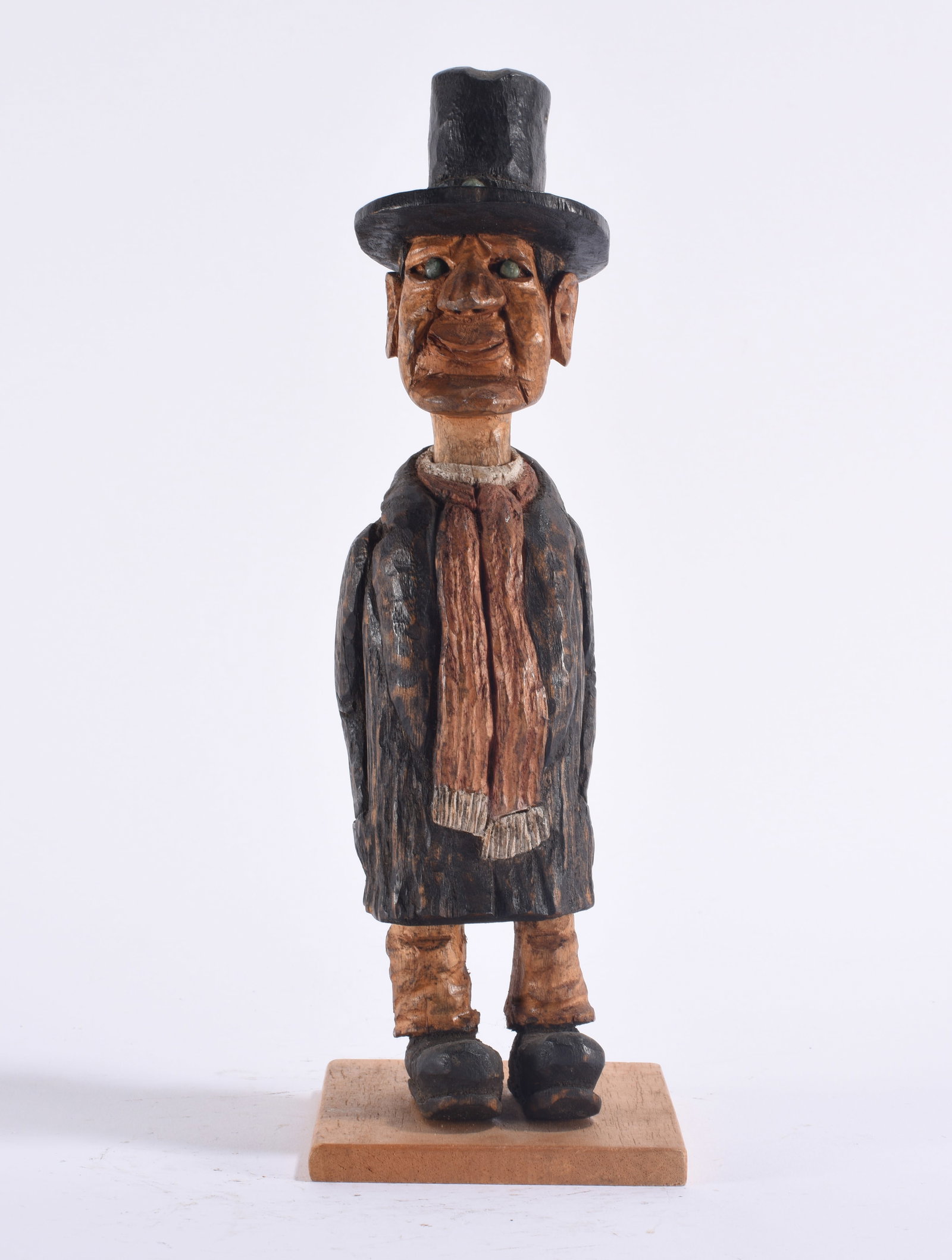 Wooden Carved Figure: American folk art carved and painted wooden figure depicting a formally dressed man wearing a tall black top hat, dark coat, scarf, trousers and oversized shoes. The elongated figure has a strongly ca