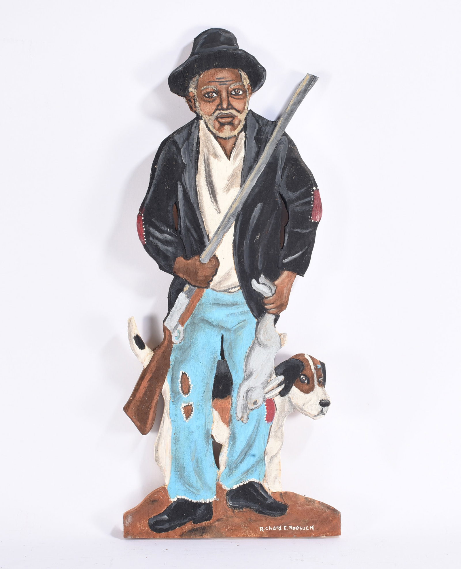 Richard Roebuck Cut Out Painted Hunter: Painted cut-out folk art figure by Richard E. Roebuck depicting an elderly hunter wearing patched blue trousers, dark jacket, and hat, carrying a long gun and game while accompanied by a hunting dog. 