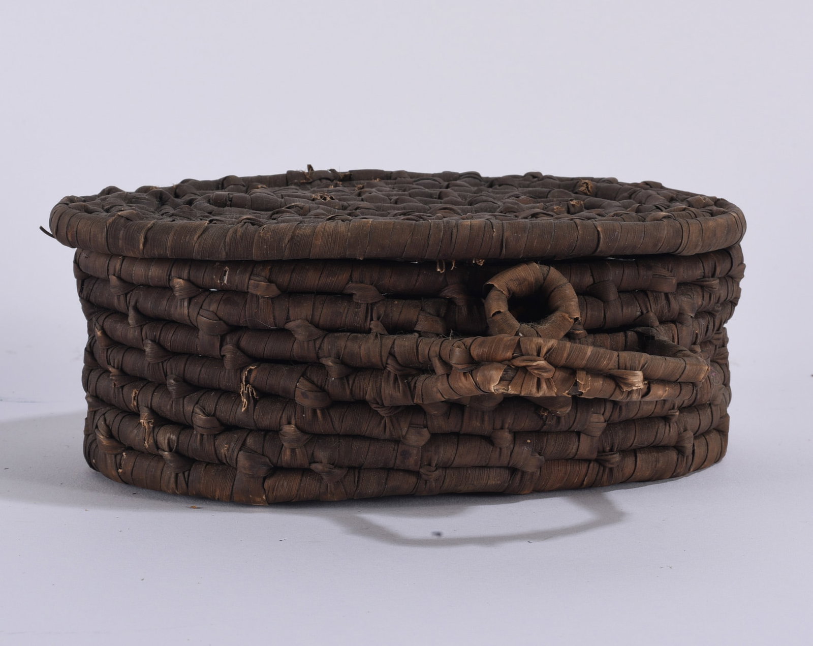 Old Gullah Geechee Sweetgrass Lidded Oval Basket: Old Gullah Geechee-style lidded oval basket constructed from dark natural plant fibers with tightly coiled and bound construction. Features a fitted lid, oval form, and small loop and wrapped
