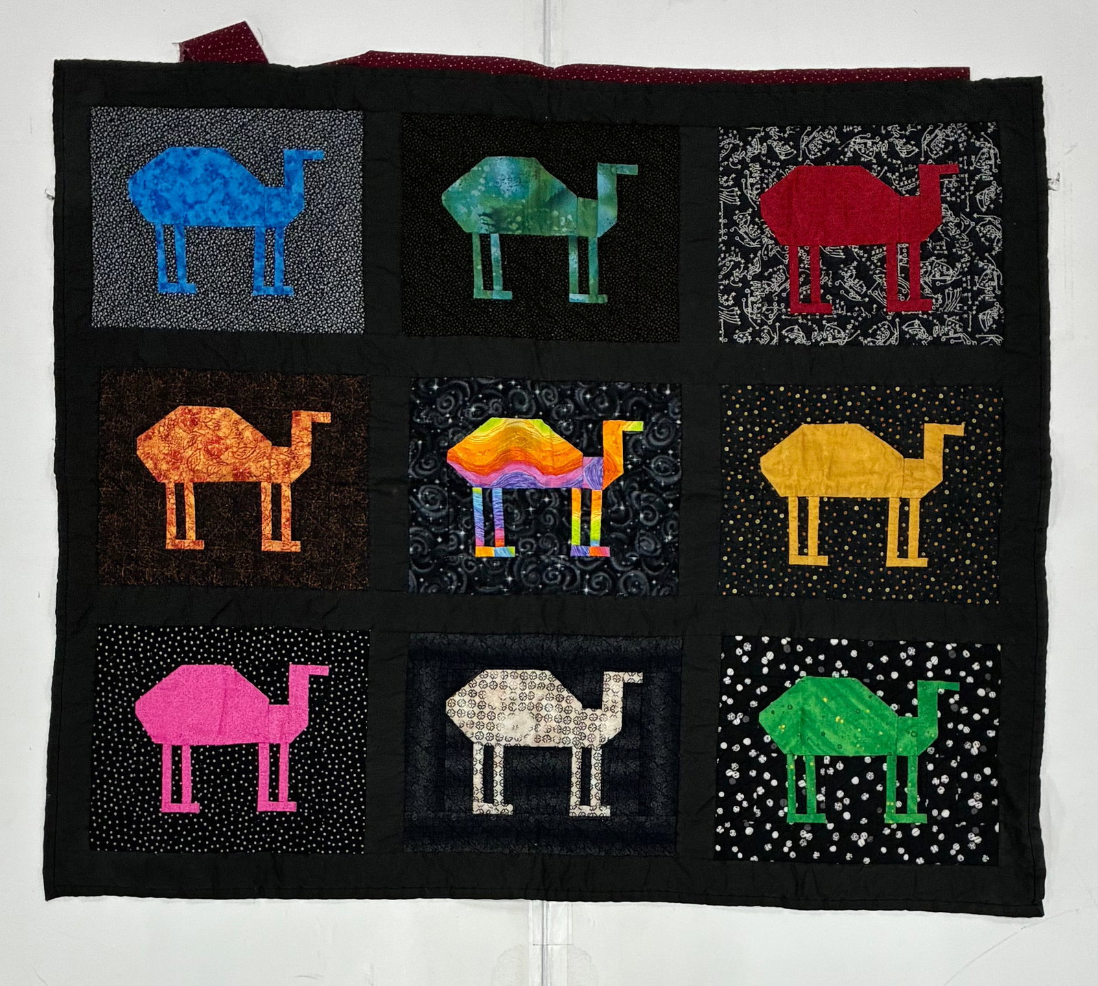 American Folk Art Camel Appliqué Quilt: 47"x40" Whimsical American folk-art appliqué quilt featuring nine stylized camels individually worked in brightly colored fabrics and arranged within black-bordered rectangular blocks. Each camel is 