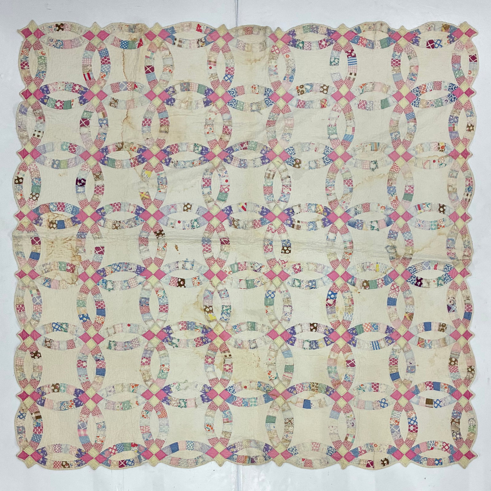 American Double Wedding Ring Scrap Quilt, Circa 1930-1940: 77"x77" American Double Wedding Ring quilt constructed from hundreds of small printed cotton scraps forming interlocking pieced rings against a cream ground. Pink and pale yellow joining squares punct