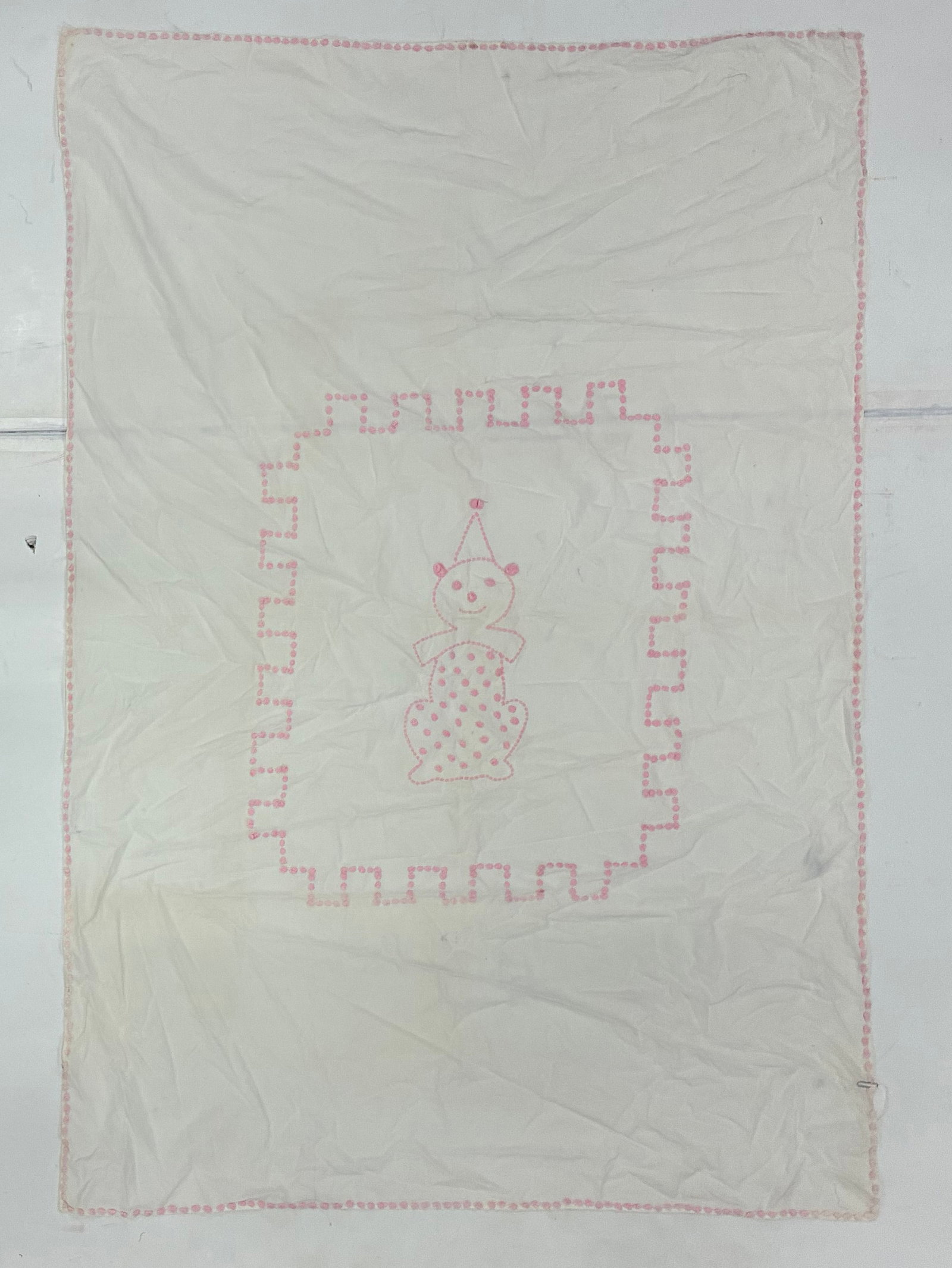 American Pinkwork Embroidered Child's Quilt with Clown Figure: 63"x43" American embroidered child's quilt or coverlet worked primarily in white cotton with delicate pink embroidery. A whimsical central clown or doll-like figure with pointed cap and polka-dot cost
