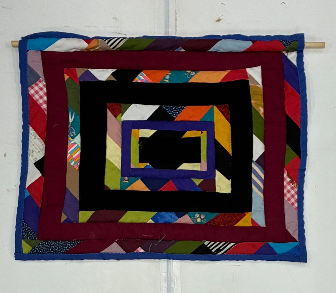 Gees Bend Miniature Quilt: 25"x21" American folk-art patchwork textile constructed as a series of concentric rectangular frames in black, burgundy, purple and brightly colored scrap fabrics. Narrow pieced bands incorporate tria