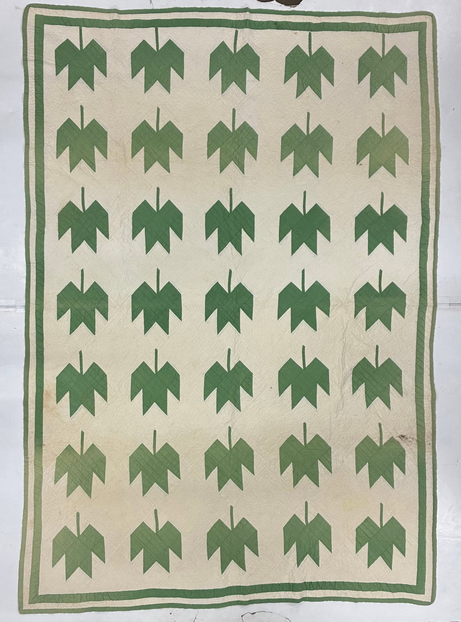 Early 20th Century American Green Leaf Appliqué Quilt: 91"x65" Early 20th century American appliqué quilt featuring thirty-five stylized green leaf motifs arranged in seven orderly rows against a cream ground. Each highly simplified leaf is formed from a