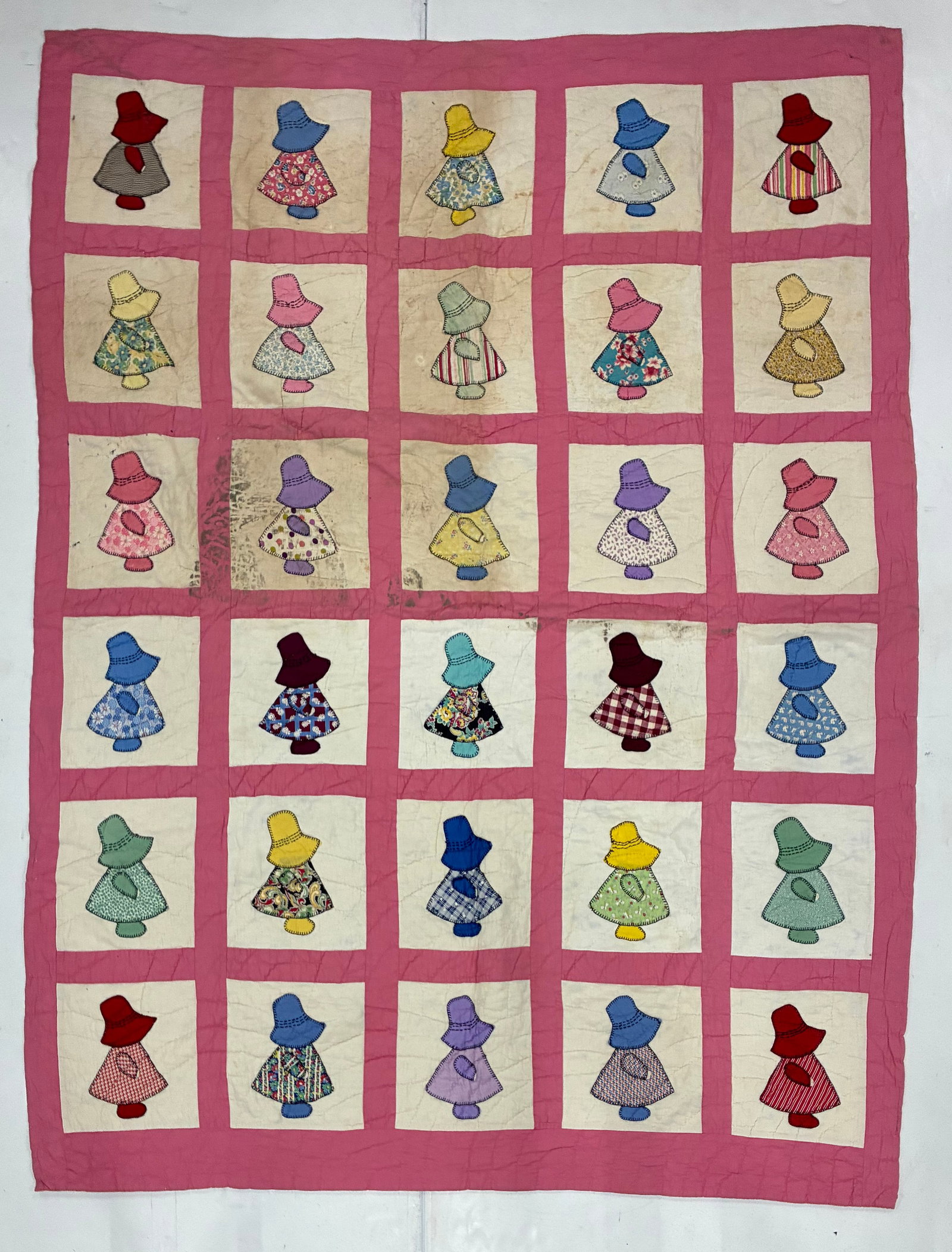 American Sunbonnet Sue Appliqué Quilt with Pink Sashing: 66"x81" American Sunbonnet Sue appliqué quilt featuring thirty individually worked bonneted figures arranged in six rows against cream block grounds and separated by broad pink sashing. Each figure