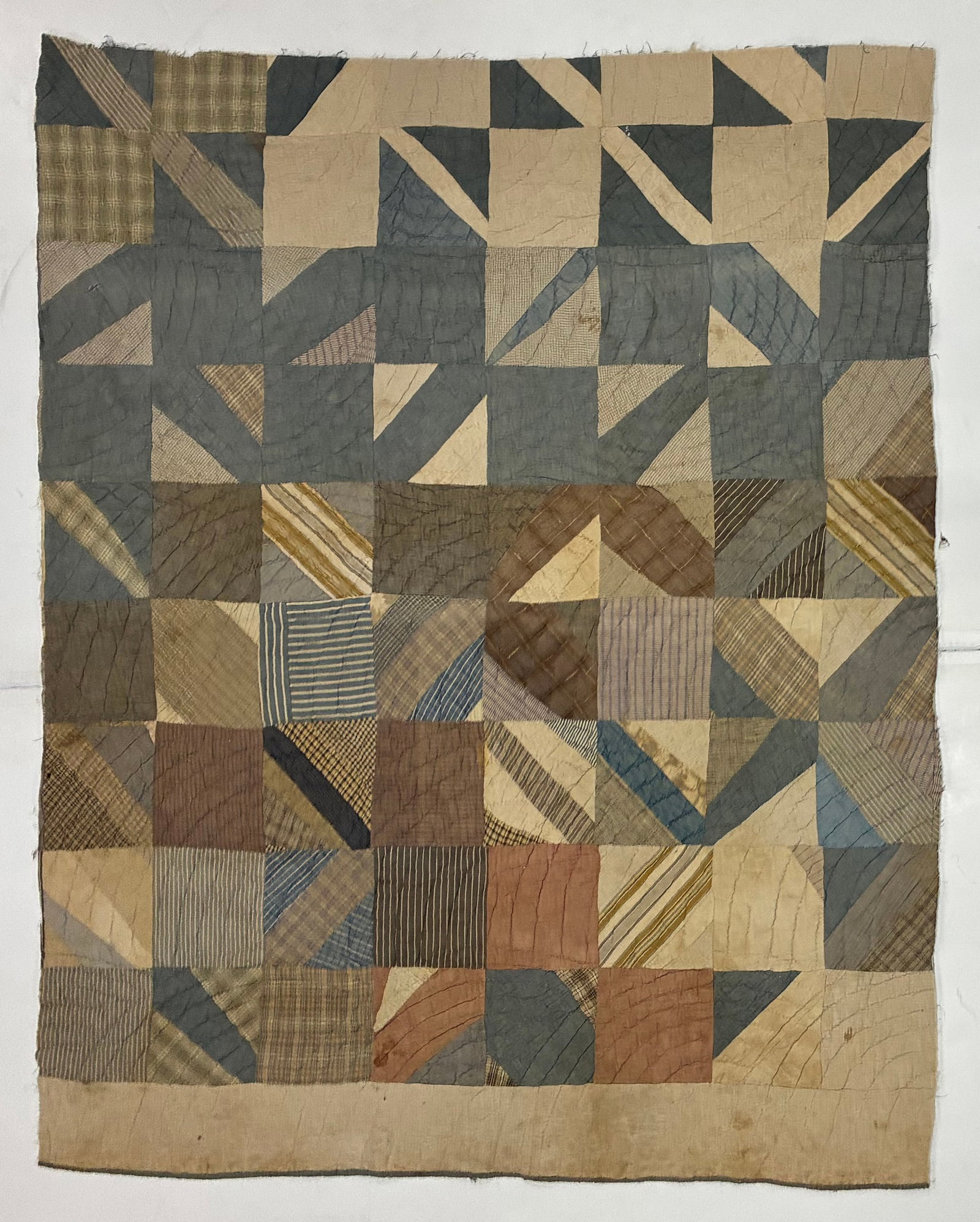 Early 20th Century American Improvisational Geometric Utility Quilt: 63"x52" Early 20th century American utility quilt composed of square blocks divided by diagonal and irregular geometric pieces in muted blue, gray, tan, brown, cream and striped fabrics. The maker