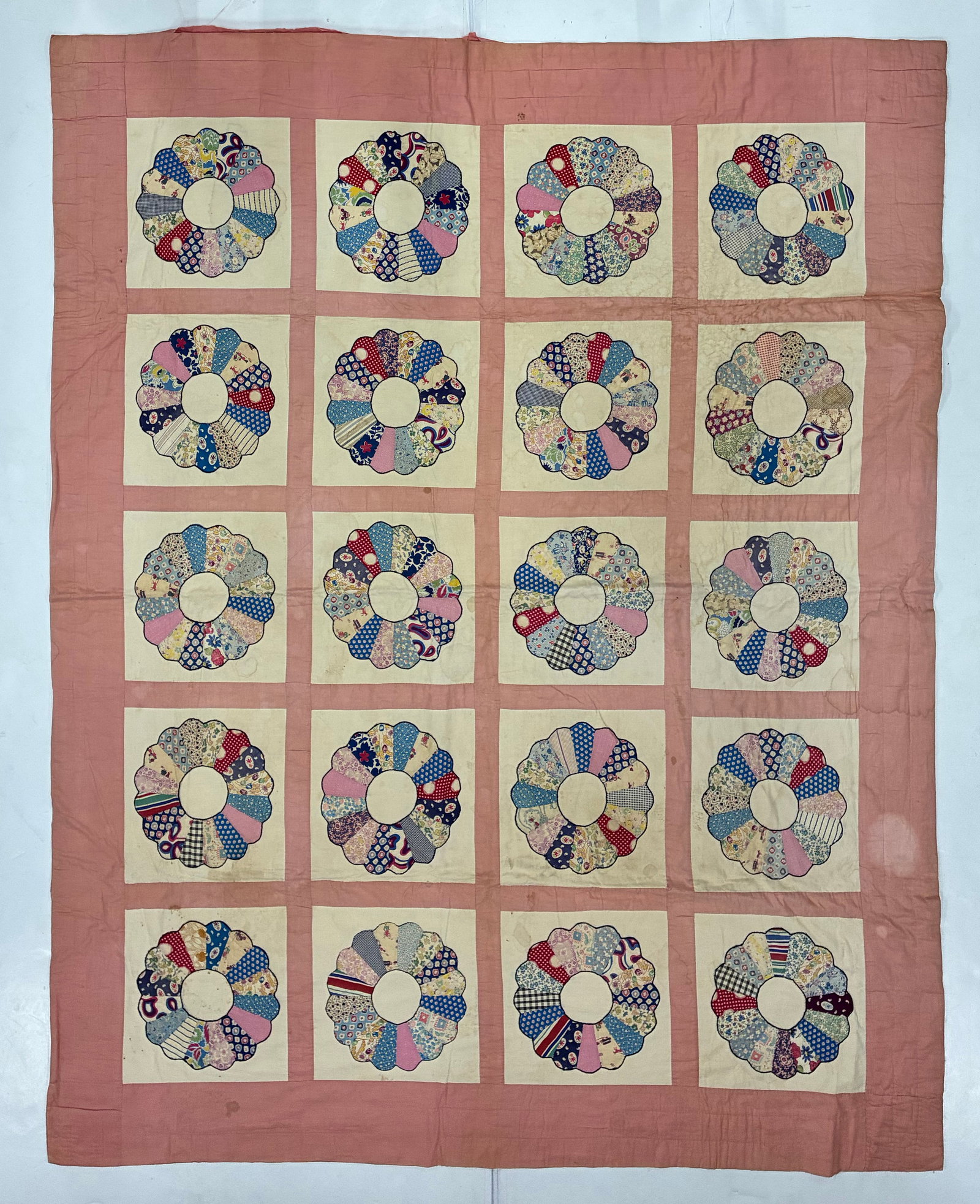 American Dresden Plate Scrap Quilt with Pink Sashing: 70"x85" American Dresden Plate quilt featuring twenty individual floral blocks arranged in five rows of four against a warm dusty-pink ground. Each plate is assembled from numerous scrap fabrics inclu