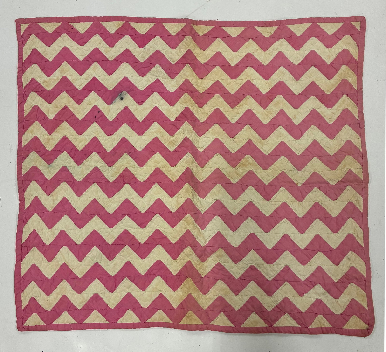 American Folk Art Pink and Cream Zigzag Quilt: 24"x20" Handmade quilt featuring repeated horizontal rows of bold pink and cream zigzag or chevron forms. The simple two-color construction creates a strong rhythmic geometric design across the