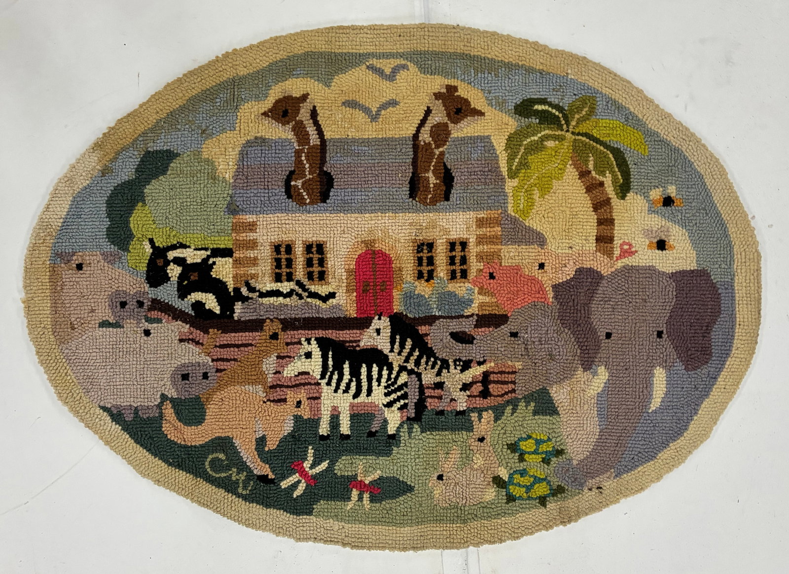 Vintage Noah’s Ark Animal Scene Hooked Rug: 36"x27" Oval hand-hooked rug depicting a fanciful animal scene surrounding a central building or ark-like structure with a red doorway. Figures include an elephant, zebra, cattle, giraffe-like