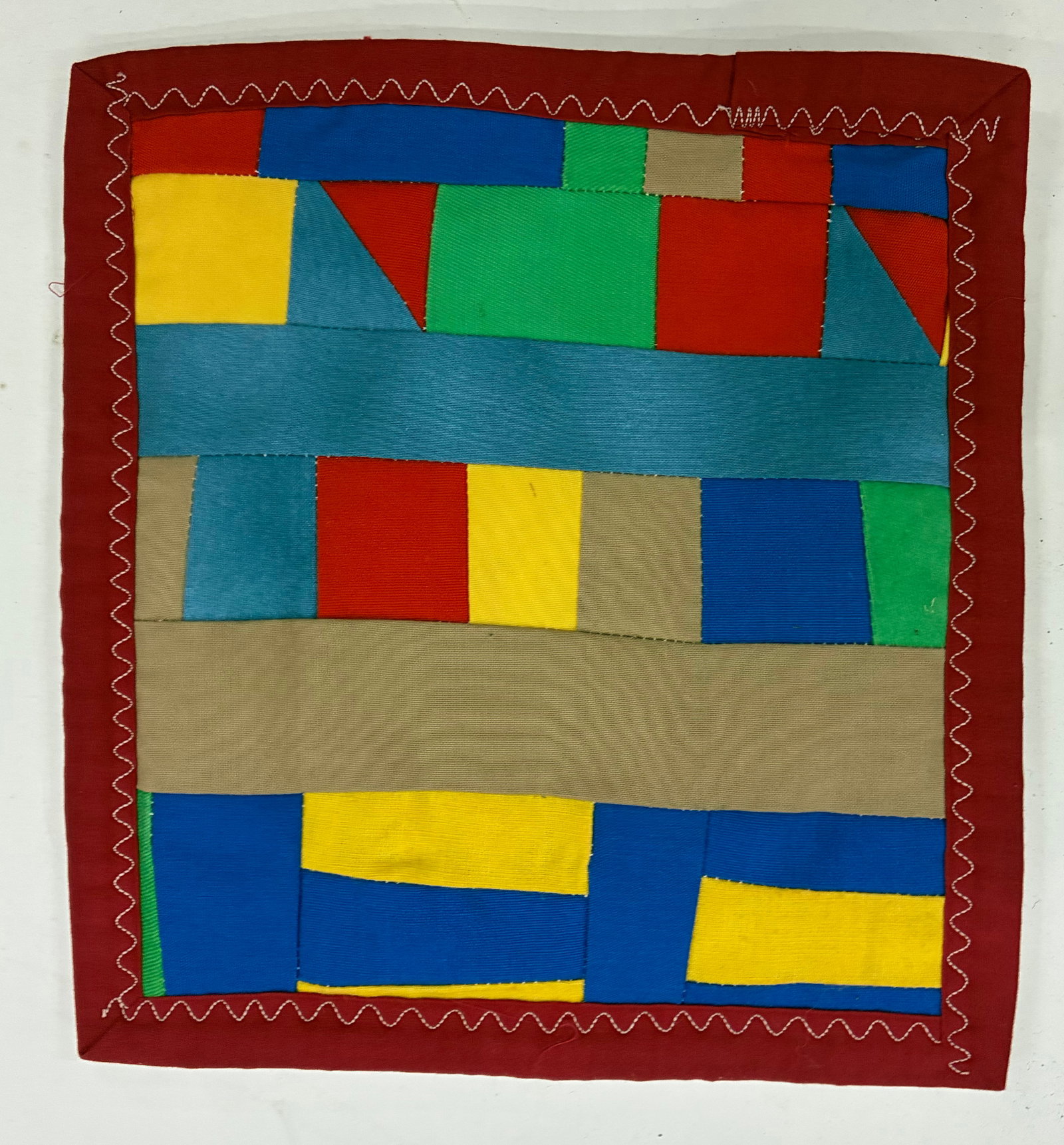 Miniature Gees Bend Quilt with stamp: 9"x10" Handmade improvisational textile composed of brightly colored rectangular and geometric fabric pieces in blue, green, yellow, red and tan. Broad horizontal strips interrupt the smaller
