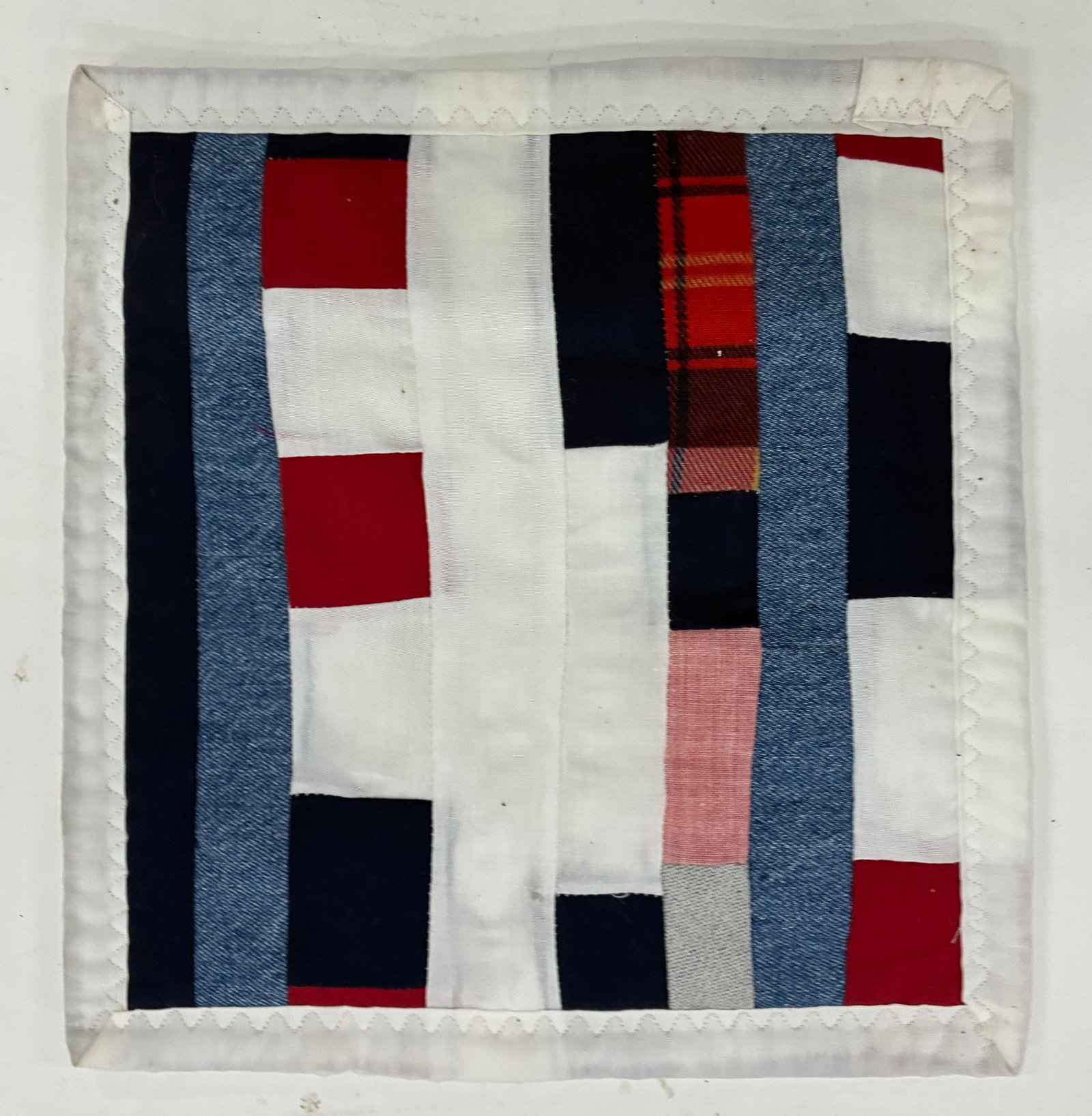 Miniature Gees Bend Quilt with stamp: 9"x10" Handmade improvisational textile assembled from vertical strips and rectangular pieces of white, navy, denim blue, red, plaid and pink fabric. Long vertical bands contrast with smaller blocks