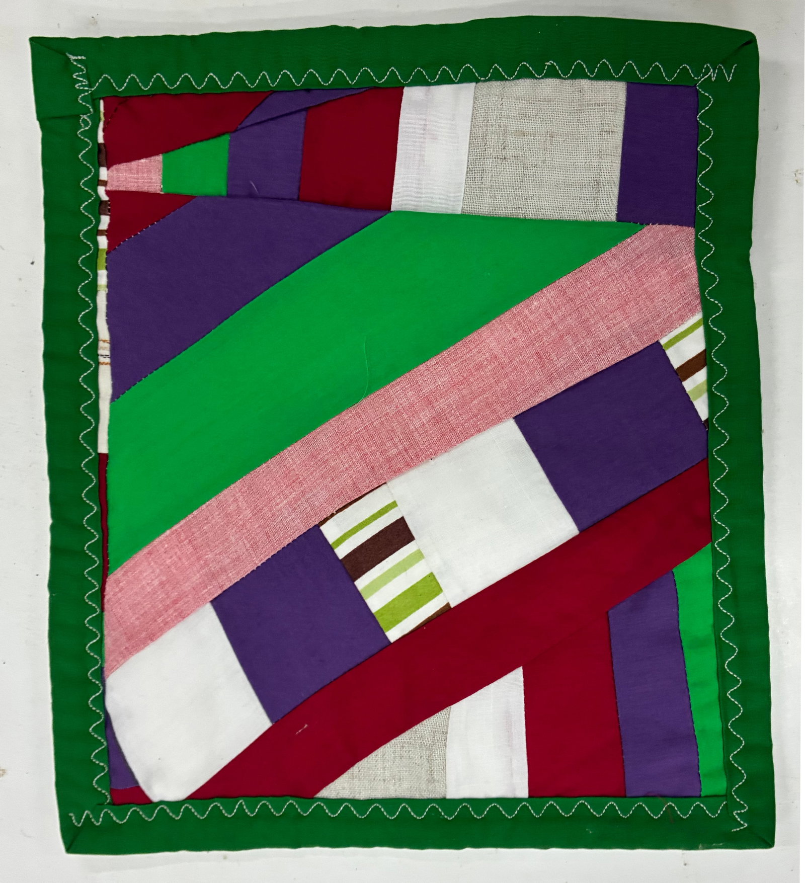 Miniature Gees Bend Quilt with stamp: 9"x10" Handmade improvisational textile assembled from broad diagonal and rectangular sections of green, purple, red, pink, white and striped fabric. Large overlapping bands create a dynamic abstract