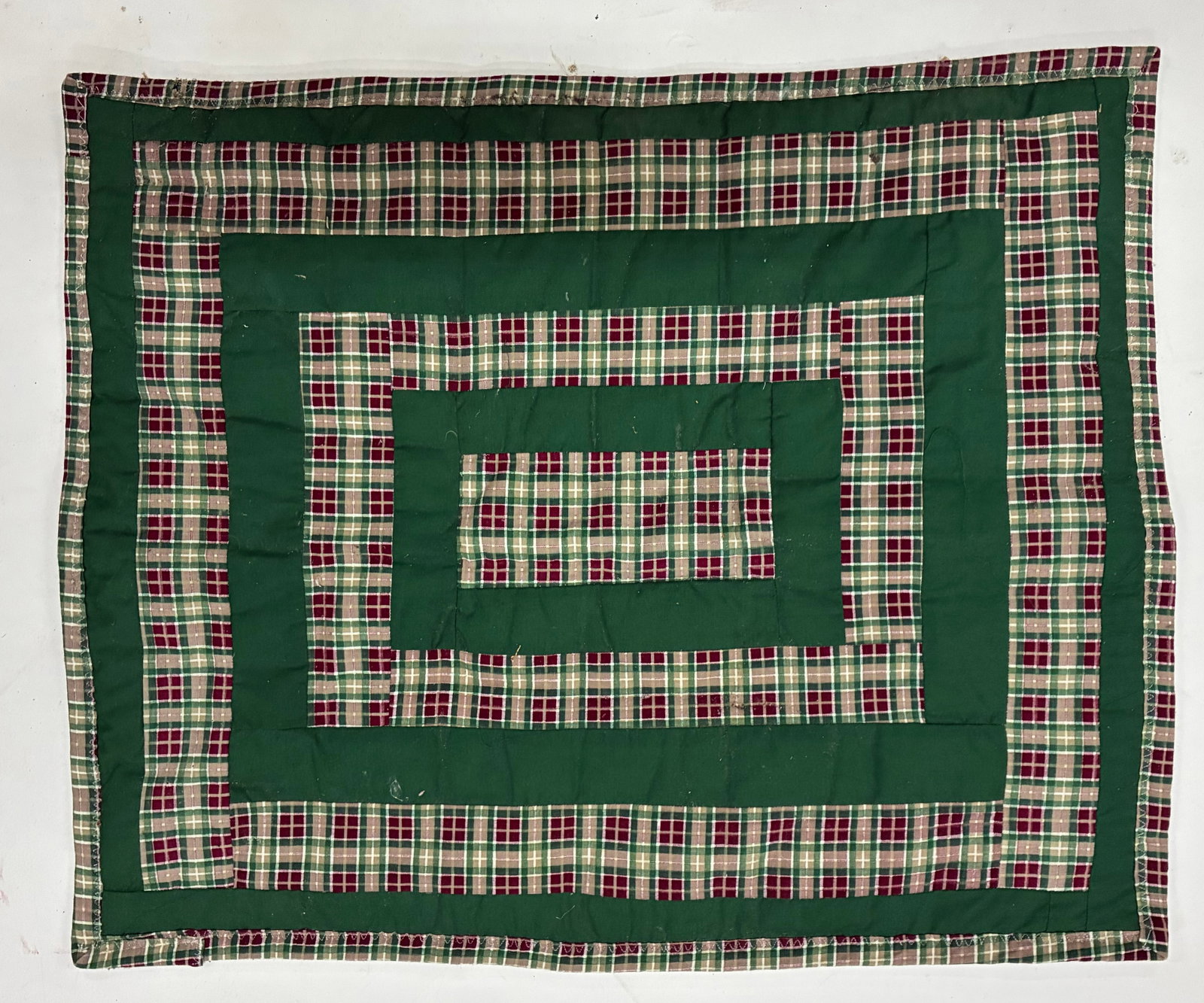 Miniature Gees Bend Quilt with stamp: 26"x21" Handmade quilt featuring alternating bands of dark green solid fabric and red, green and cream plaid arranged in a concentric rectangular or log cabin format. The repeated bands create a