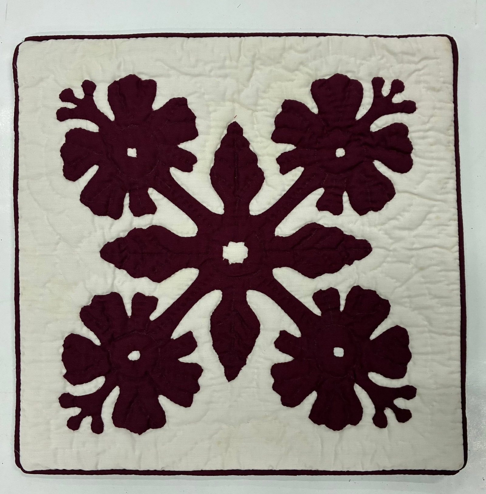 American Folk Art Hawaiian Applique Miniature Floral Quilt: 12"x12" Handmade appliqué quilt featuring four large burgundy floral motifs arranged symmetrically on a cream ground. Each stylized blossom is connected through a central branching floral and leaf