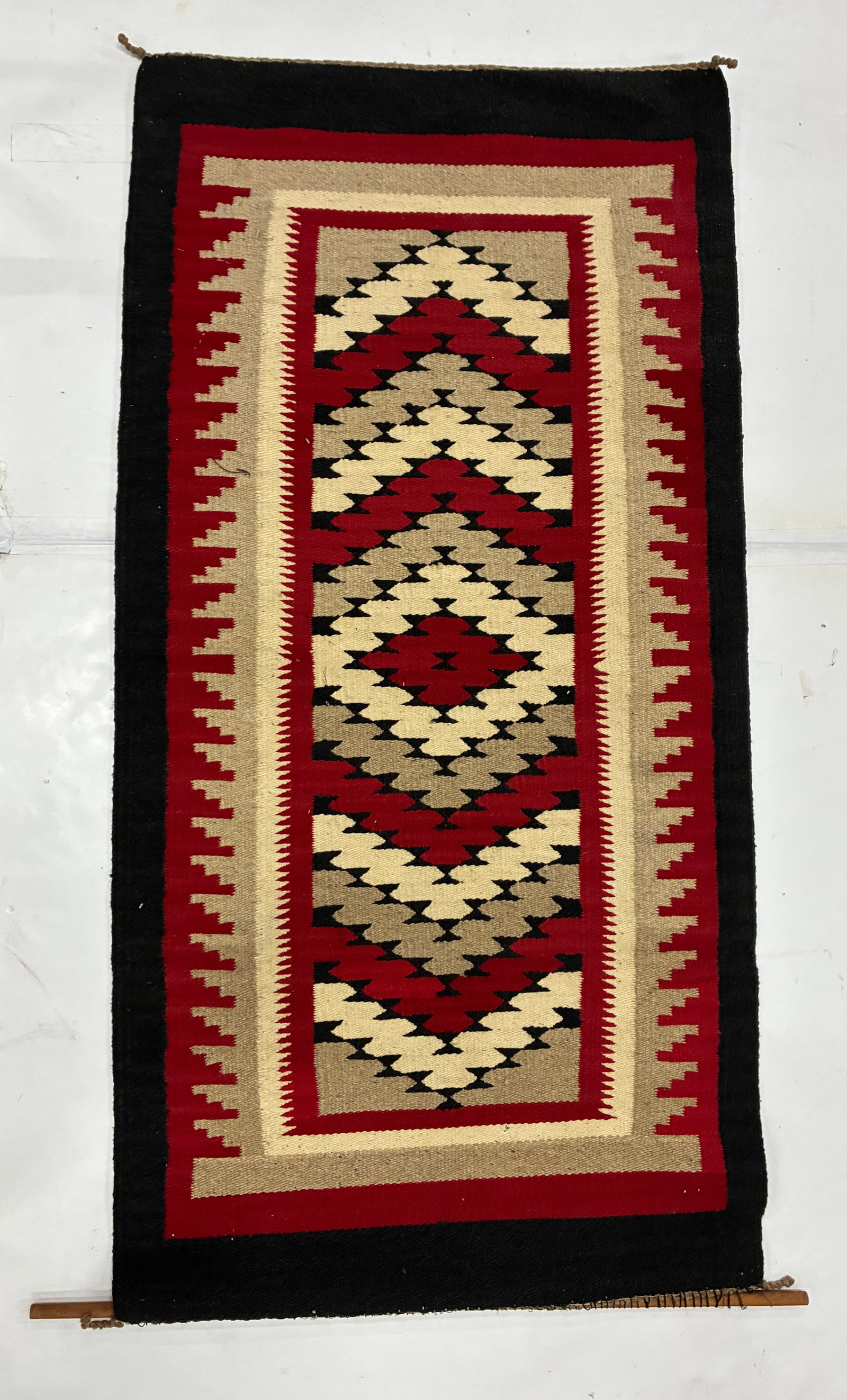 Vintage Southwestern Red Black and Cream Geometric Textile: 61"x30" Handwoven textile featuring a bold central arrangement of stepped diamonds and triangular geometric forms in red, black, cream and tan. Multiple patterned borders surround the central field,
