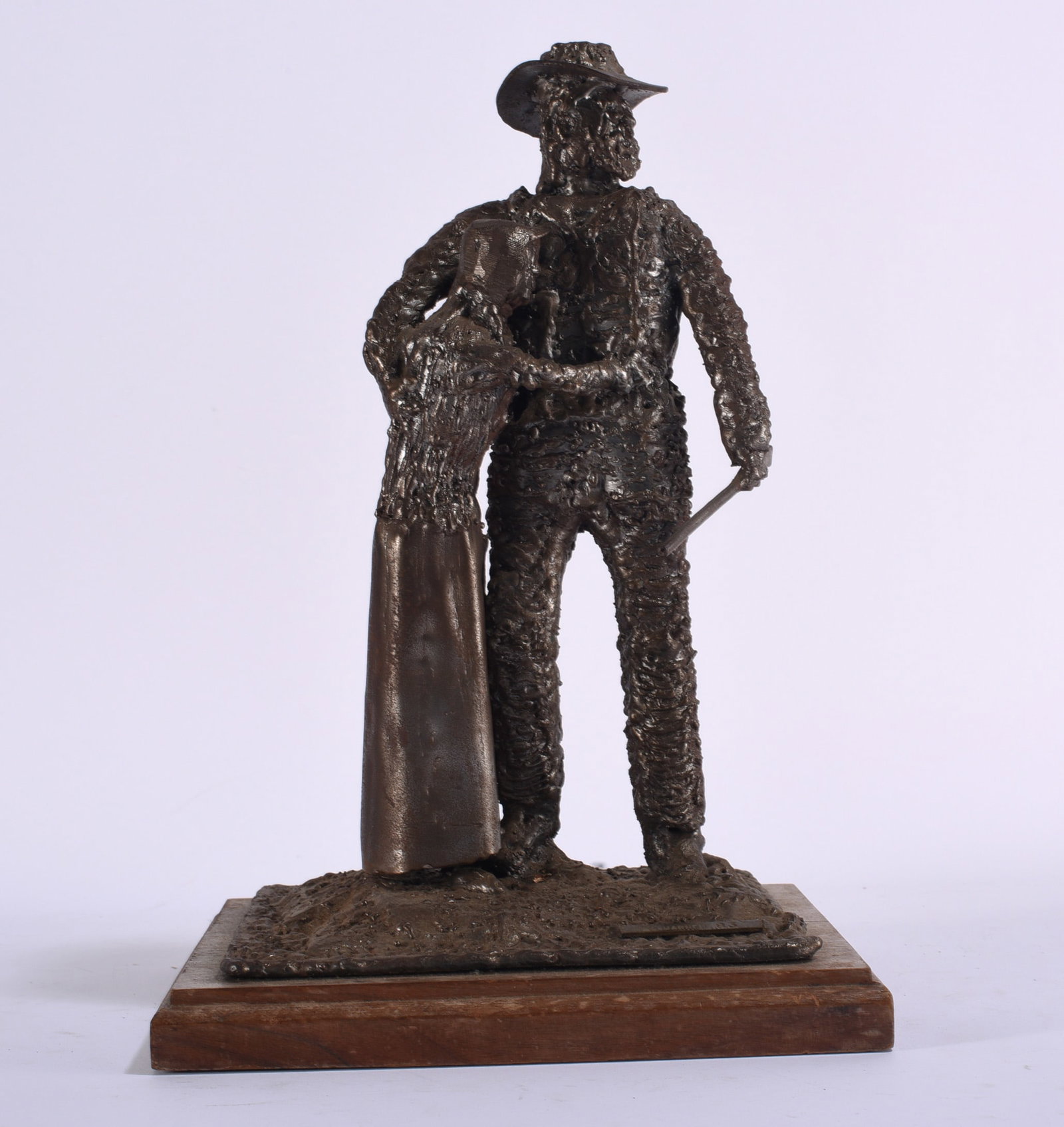 Folk Art Metal Sculpture of Farmer and Woman: 9"x9"x13" Folk art metal sculpture depicting a standing man in a broad-brimmed hat holding a tool beside a woman. Constructed with heavily textured welded or modeled metal surfaces and finished in a d