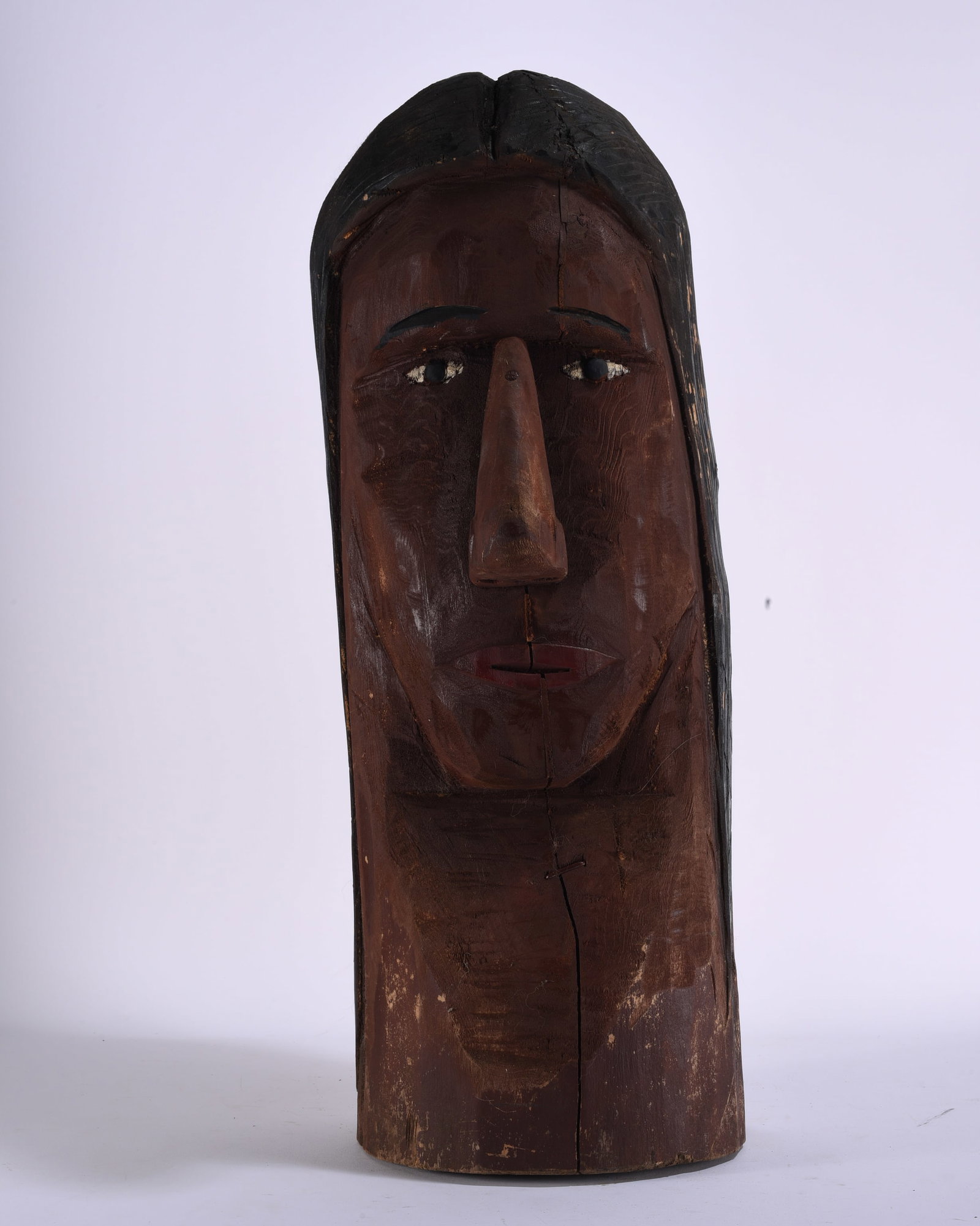 Large Folk Art Carved Wooden Face Sculpture: 9"x24" Large primitive folk art face sculpture carved from a single section of wood with elongated form, deeply carved facial features, projecting nose, inset eyes and black-painted hair. Dark brown p