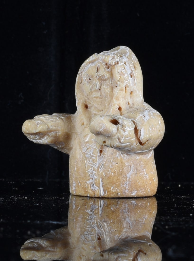 Inuit Carved Bone Hunter Figure: 1" Inuit carved bone figural sculpture depicting a bundled hunter with arms extended forward. Hand carved with simplified facial and clothing details, retaining warm natural coloration, surface wear a