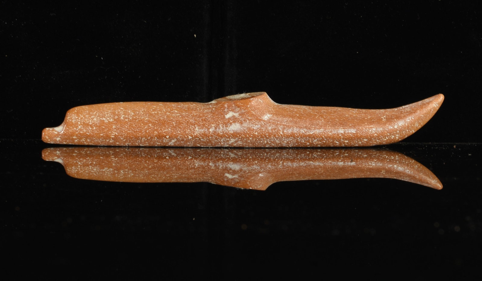 Inuit Carved Bone Kayak Model: 5"x.5" Inuit carved bone miniature kayak model with long narrow hull, raised center section and gracefully upturned end. Warm reddish-brown coloration with natural surface variation.