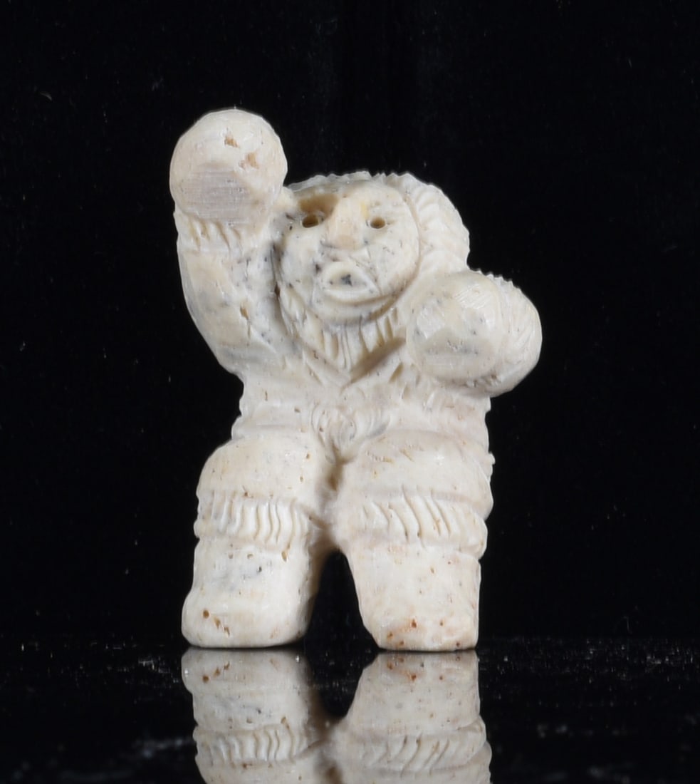 Inuit Carved Bone Hunter Figure: 1" Inuit carved bone hunter figure wearing traditional cold-weather clothing with one arm raised and the other extended. Hand carved with facial details, heavy boots and incised garment decoration.