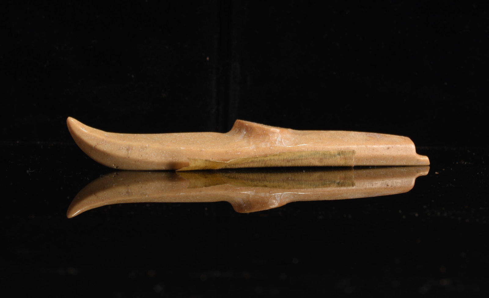 Inuit Carved Bone Kayak Model: 5"x.5" Inuit carved bone miniature kayak model with long narrow hull, raised center section and upturned end. Smooth warm brown surface with subtle natural variation.