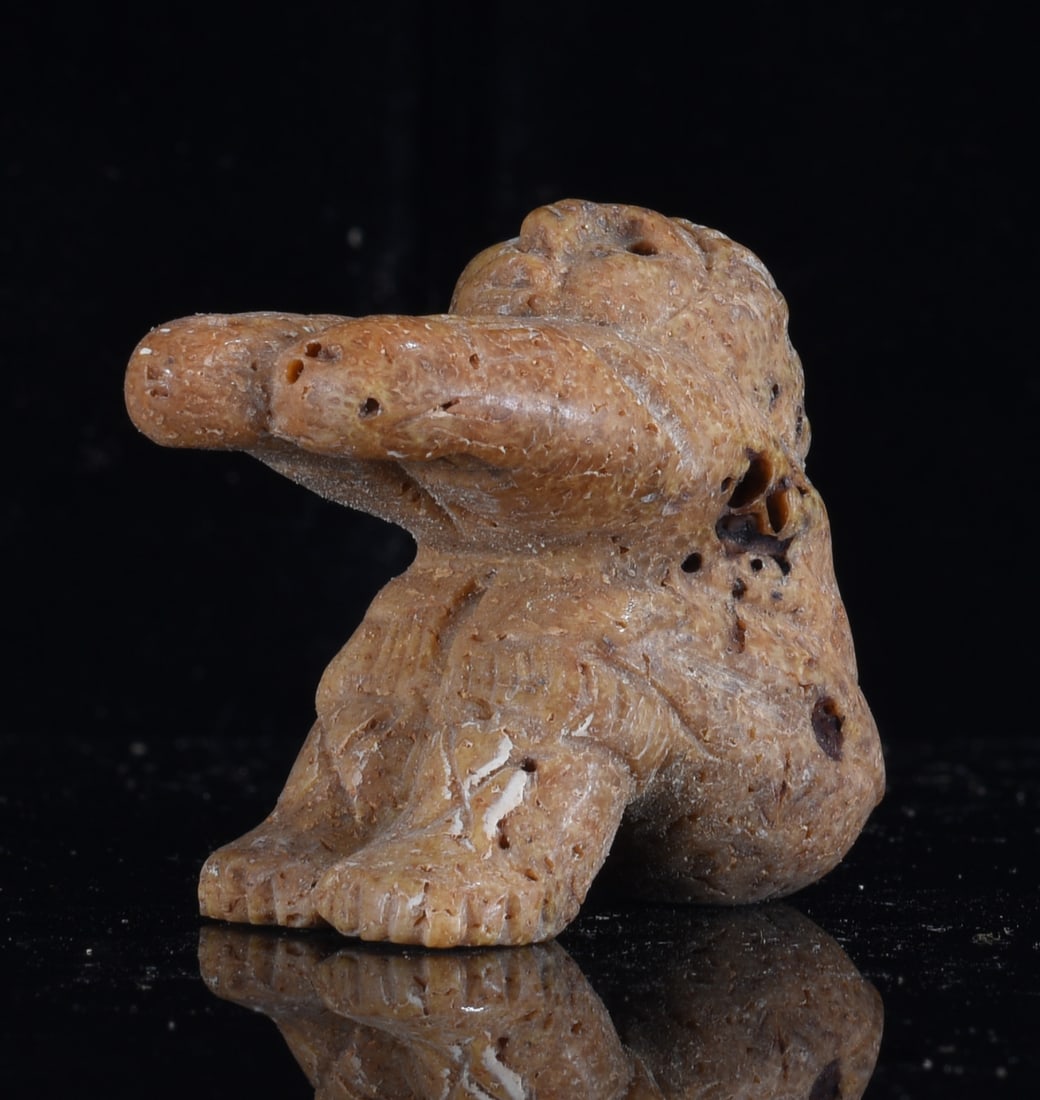 Inuit Carved Bone Seated Hunter Figure: 1" Inuit carved bone seated hunter figure with an extended arm, bent legs and deeply carved facial and garment details. Warm brown surface with extensive natural porous texture, age-related wear and p