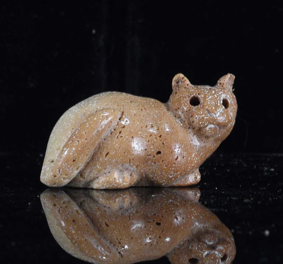 Inuit Carved Bone Arctic Fox Figure: 1" Inuit carved bone Arctic fox figure in a crouching position with pointed ears, long full tail and drilled eyes. Warm brown coloration with natural porous texture and surface wear.
