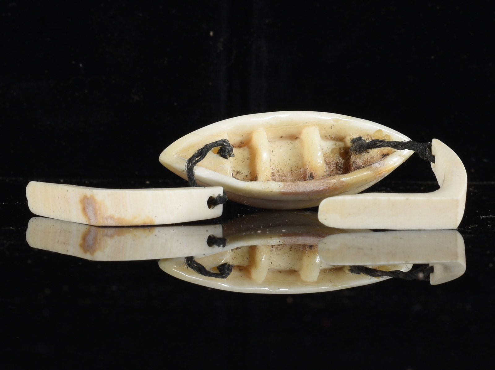 Inuit Carved Bone Umiak Boat Model with Paddles: 3" Inuit carved bone miniature umiak or open boat model accompanied by two loose paddles. Cream-colored carved construction with interior ribs and cord attachments, showing natural discoloration and a