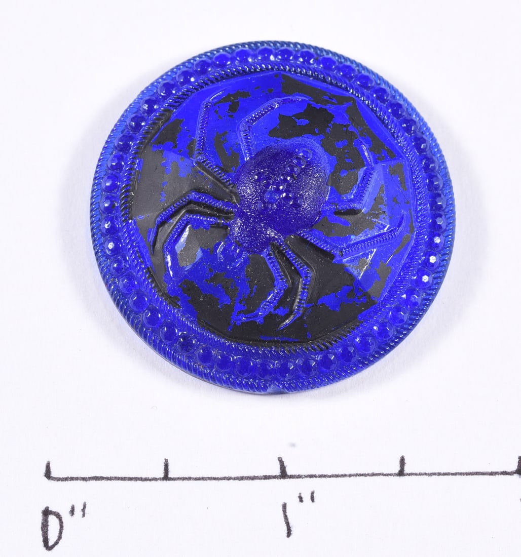 Antique Cobalt Blue Glass Spider Pictorial Button: Large antique cobalt blue pressed glass pictorial button featuring a raised spider surrounded by a molded beaded border with contrasting black decoration. Integral molded glass self-shank to reverse. 