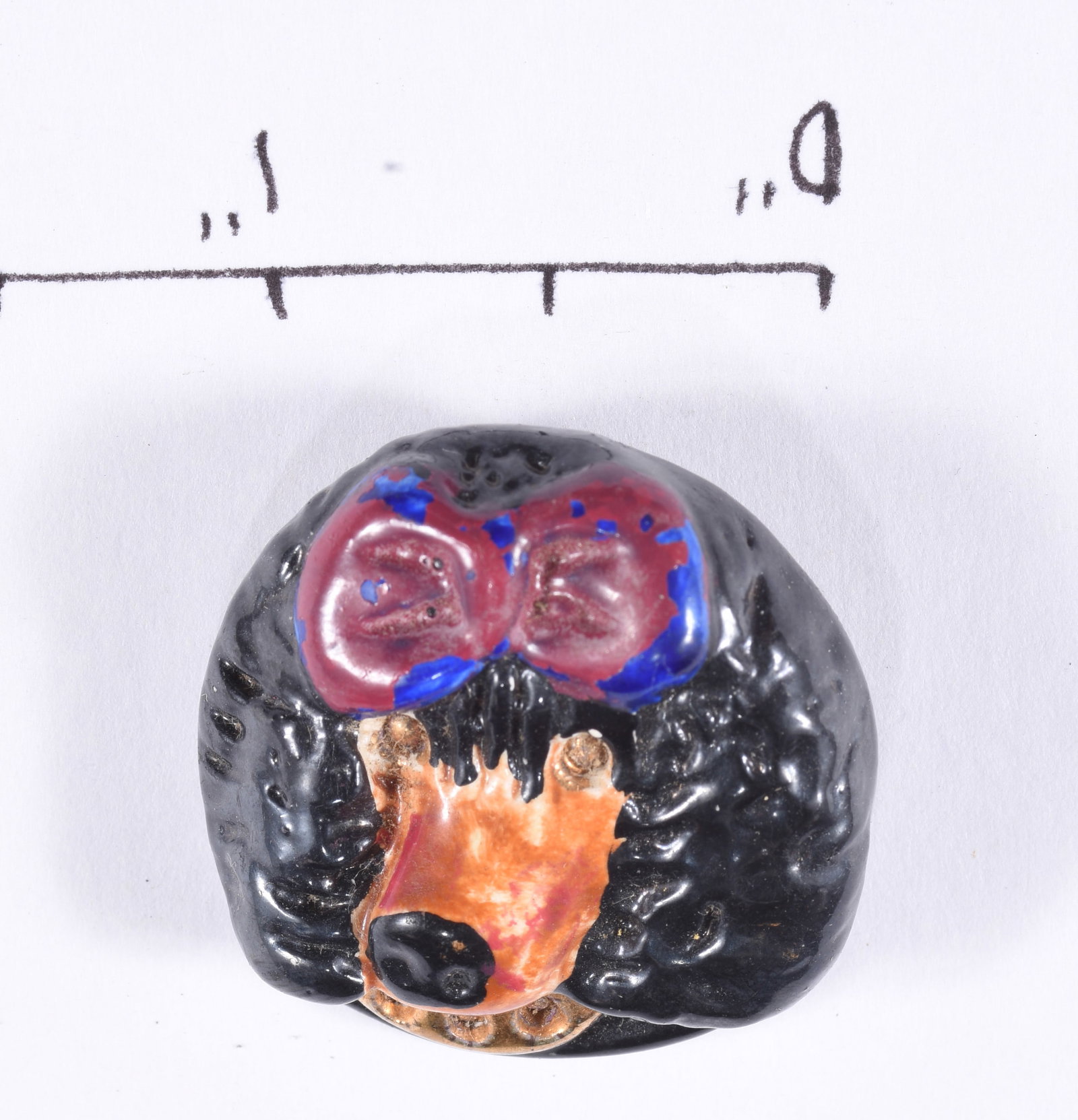 Vintage Black Figural Bear Button: Unusual large black molded figural button depicting a stylized human or theatrical mask with raised facial features and applied orange, red and blue decoration. Metal loop shank on reverse. Circa earl
