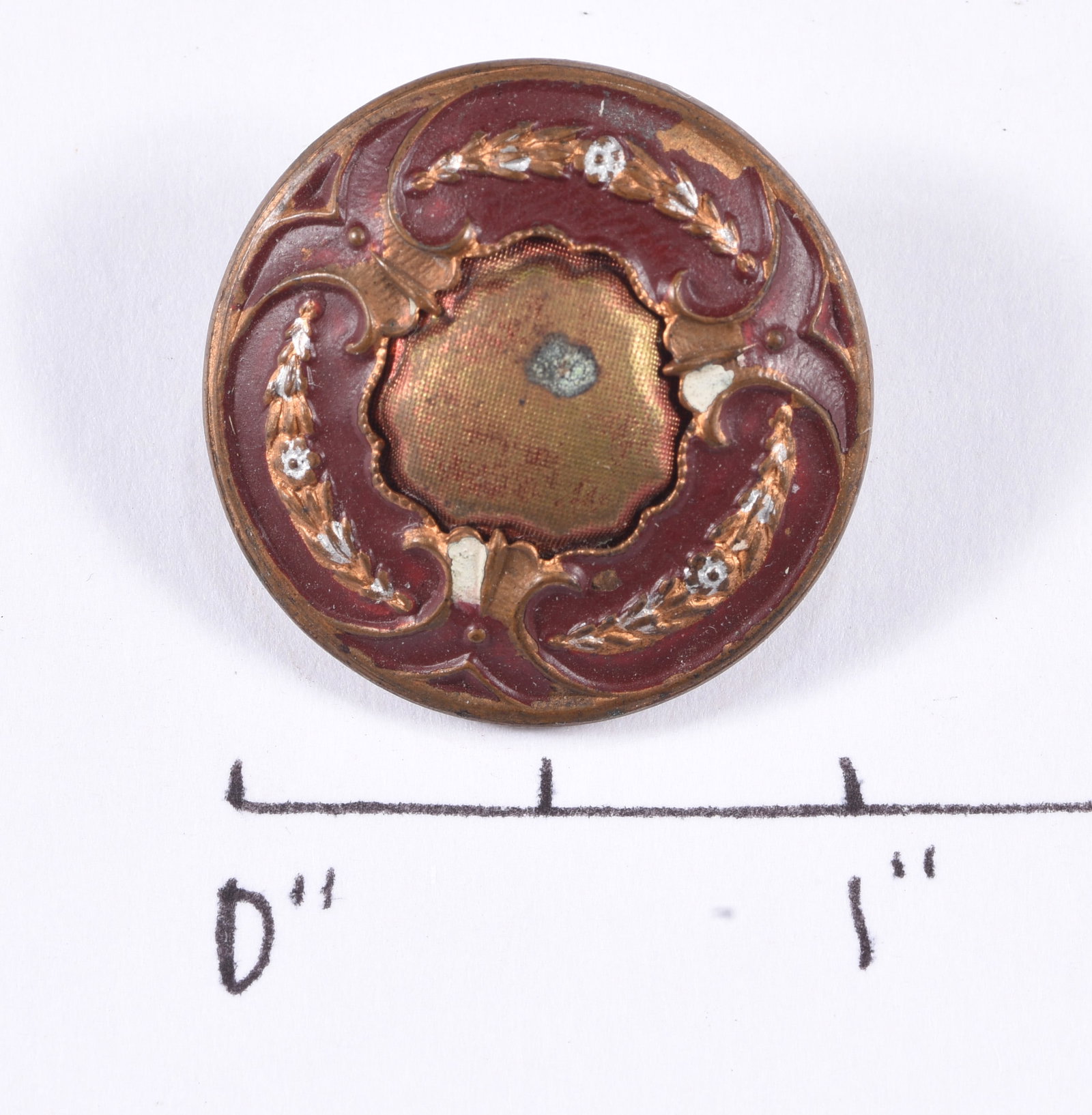 Antique Red & Copper Decorative Metal Button: Large round decorative metal button with deep red enamel or painted ground, copper-tone scrolling ornament and wreath-like decoration surrounding a recessed central panel. Metal loop shank on reverse.