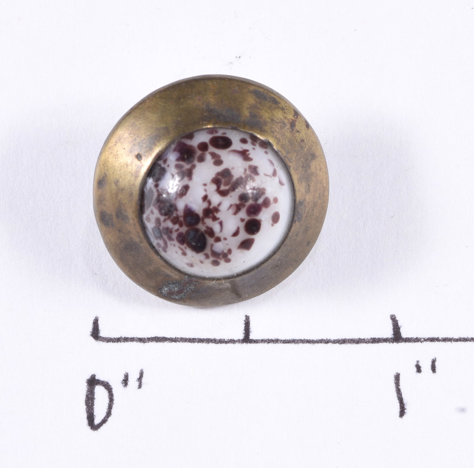 Antique Speckled Glass Set Metal Button: Round brass-tone metal button inset with a domed white glass center decorated with irregular burgundy and brown speckling. Metal loop shank on reverse. Darkened patina, oxidation and surface wear cons