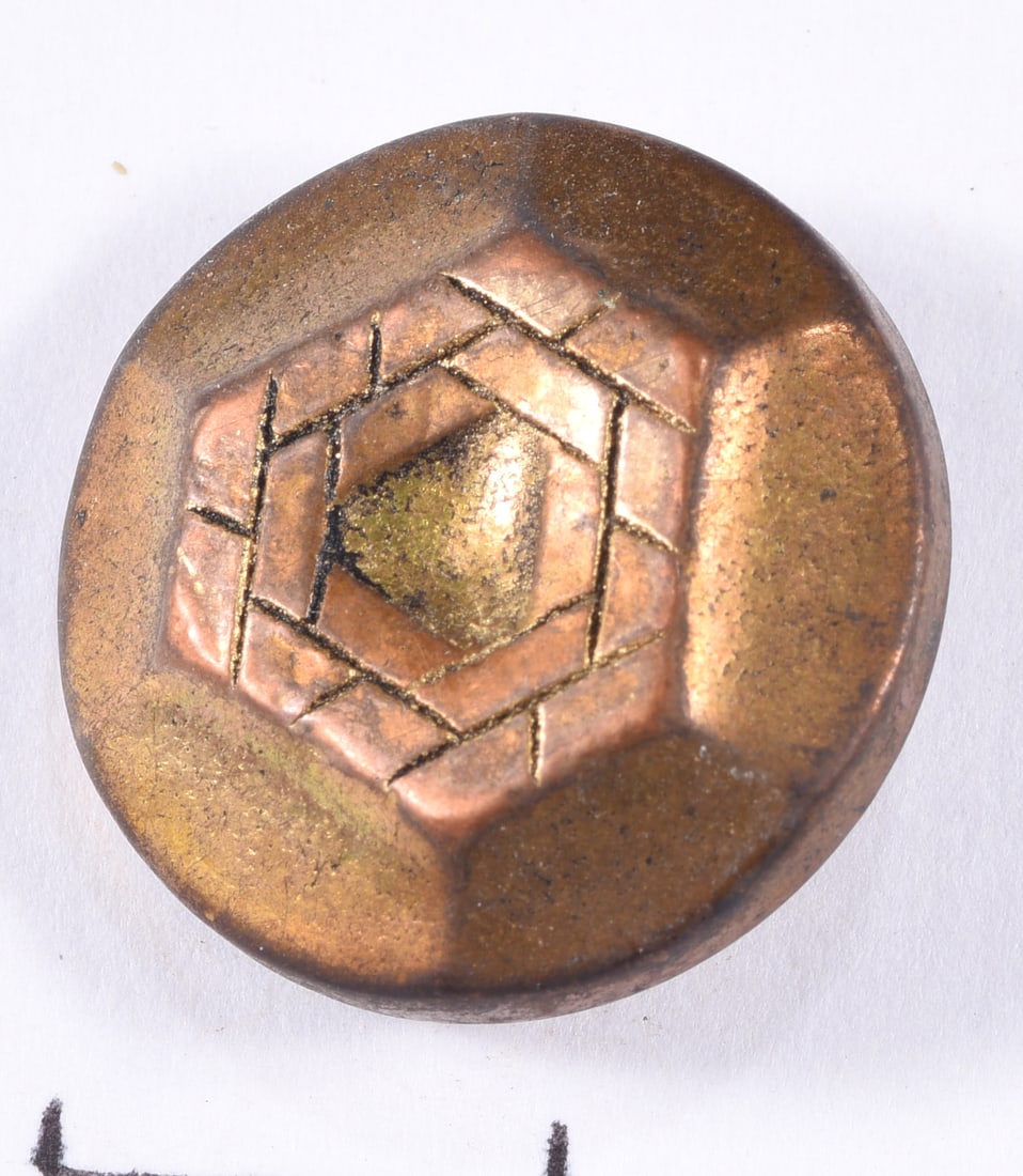 Antique Geometric Copper-Tone Metal Button: Round copper-tone metal button with raised geometric woven or basket-like central design surrounding a gilt center. Reverse fitted with shank. Warm aged patina and surface wear throughout.