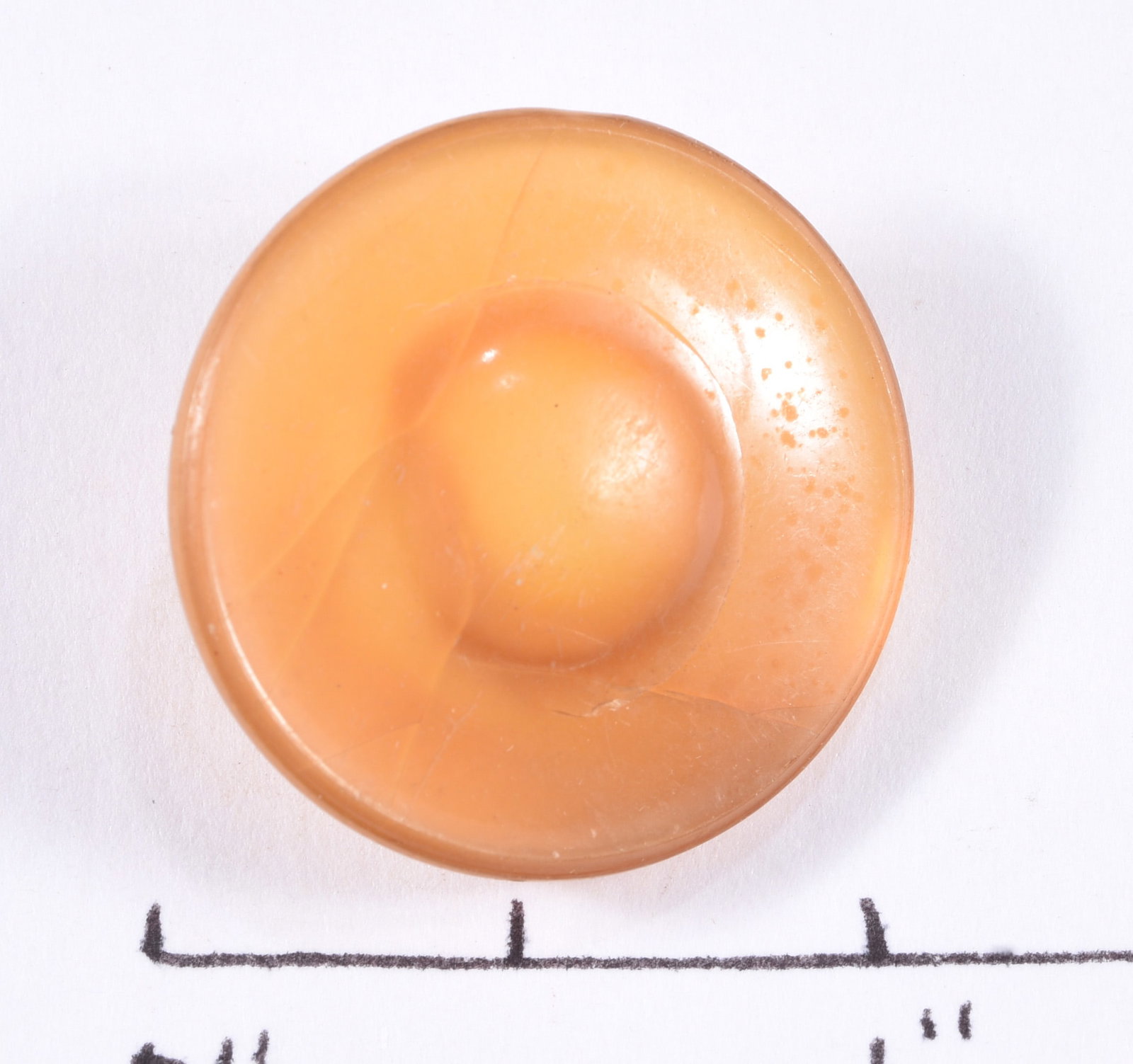 Large Peach Domed Celluloid Shank Button: Large round peach-colored celluloid or early plastic button with a deeply domed central form surrounded by a recessed border. Molded shank reverse. Light scratches and age-related surface wear.