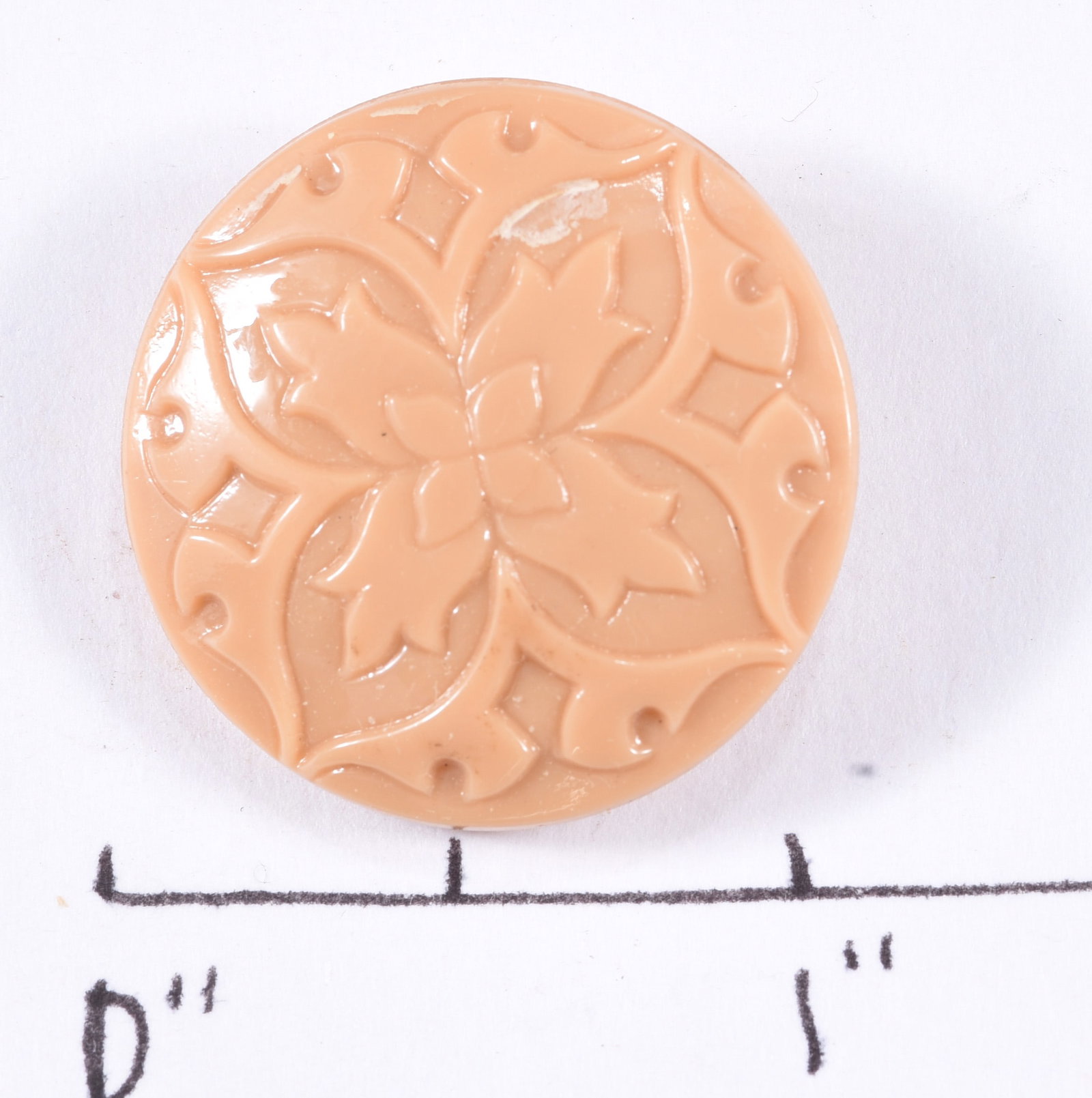 Large Vintage Peach Floral Molded Glass Button: Large vintage peach or salmon-colored molded glass button decorated with a central flower surrounded by symmetrical scrolling vines, leaves and small geometric elements. Molded self-shank to reverse. 