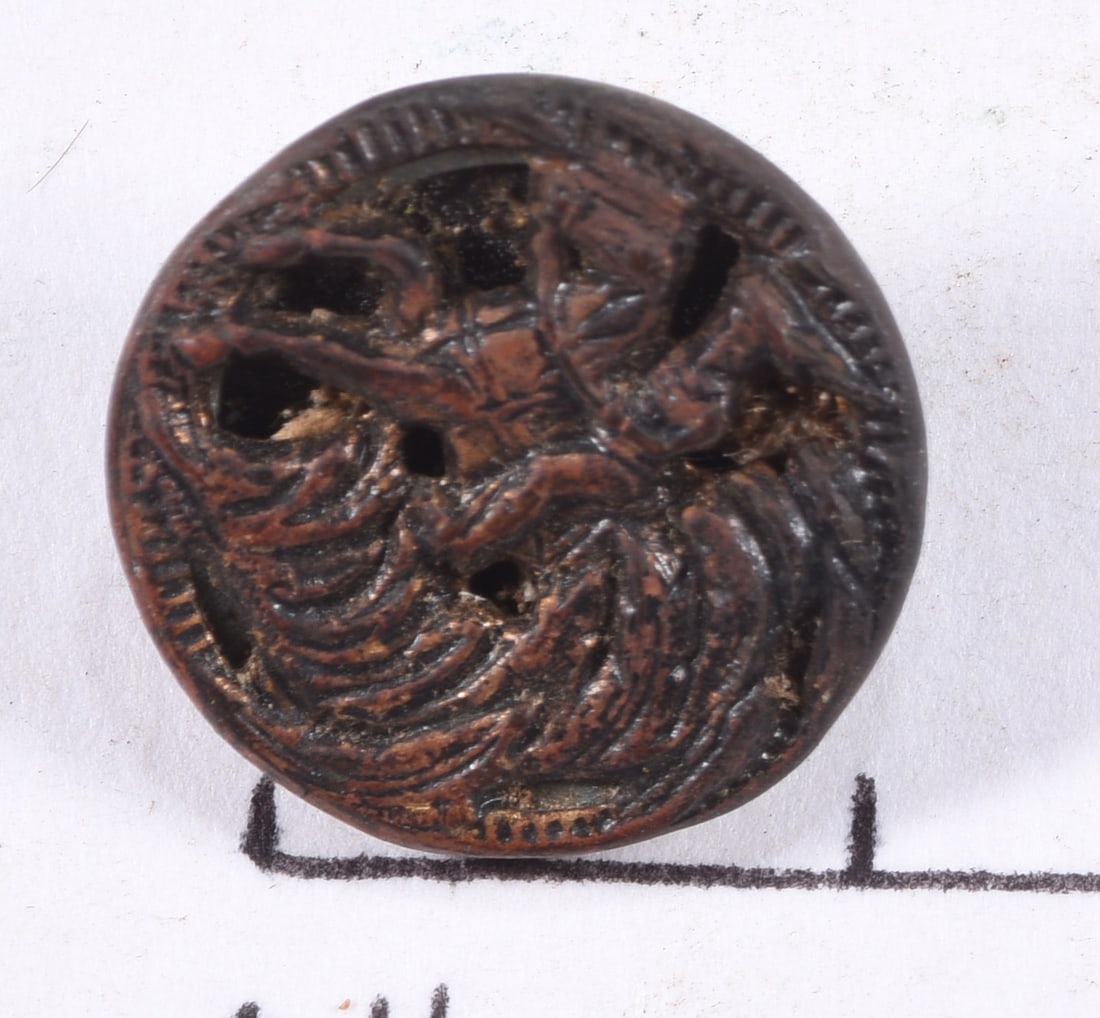 Late 19th Century Openwork Horse and Rider Button: Late 19th-century openwork picture button depicting a mounted figure or horseman on horseback surrounded by scrolling decorative elements. Pierced relief metal face over a dark contrasting backing, wi