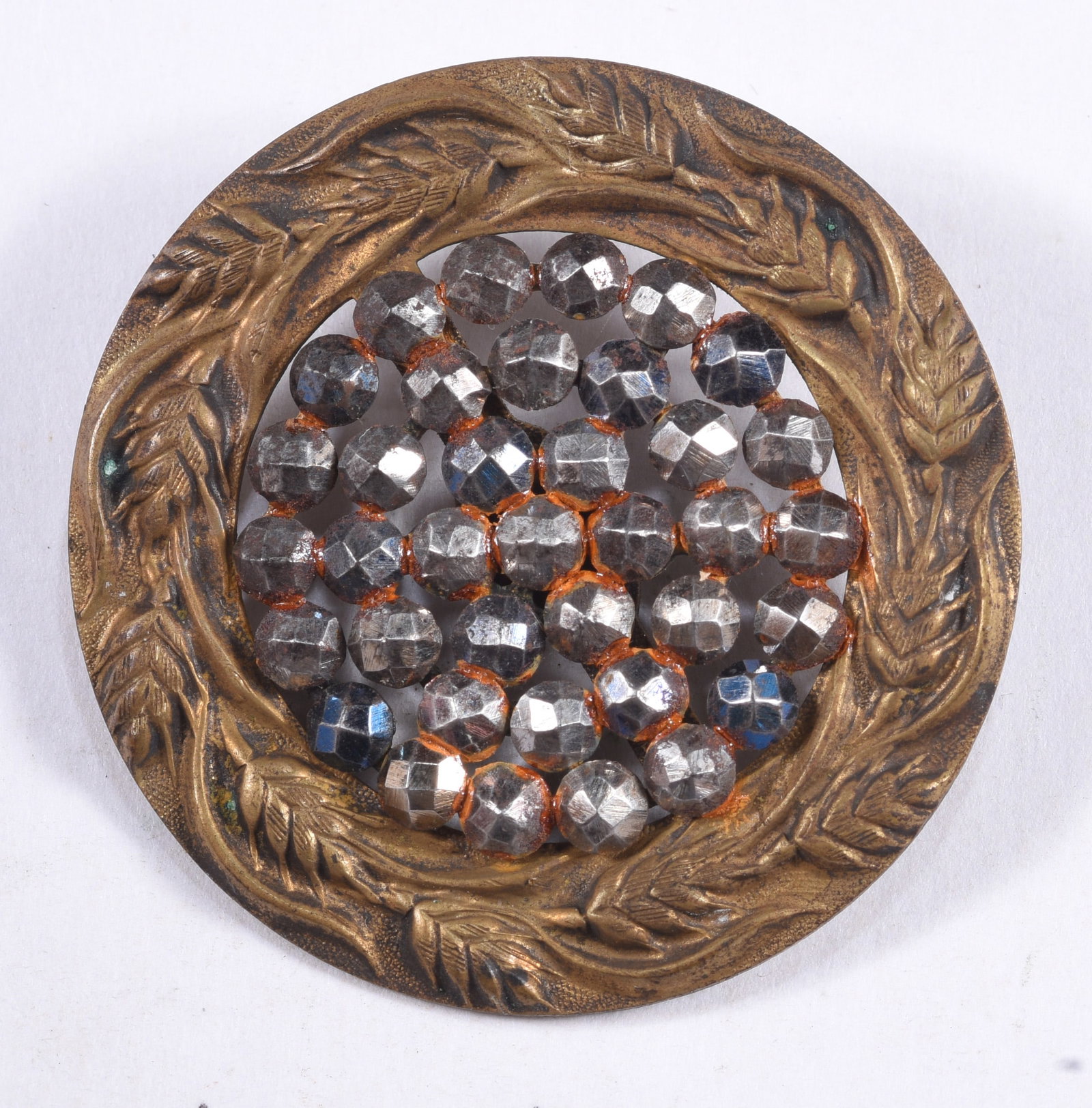 Large Antique Cut-Steel and Brass Button: Large antique round brass-tone button or ornament featuring a molded wheat or leaf border surrounding numerous faceted cut-steel elements arranged across an openwork center. Displays age-related