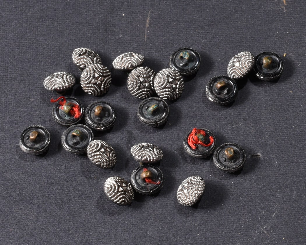 Collection of Silver-Tone & Black Decorative Buttons: Collection of approximately twenty small decorative buttons comprising ornate silver-tone textured examples and black-backed shank buttons. Silver-tone examples feature repeating beaded arcs and centr