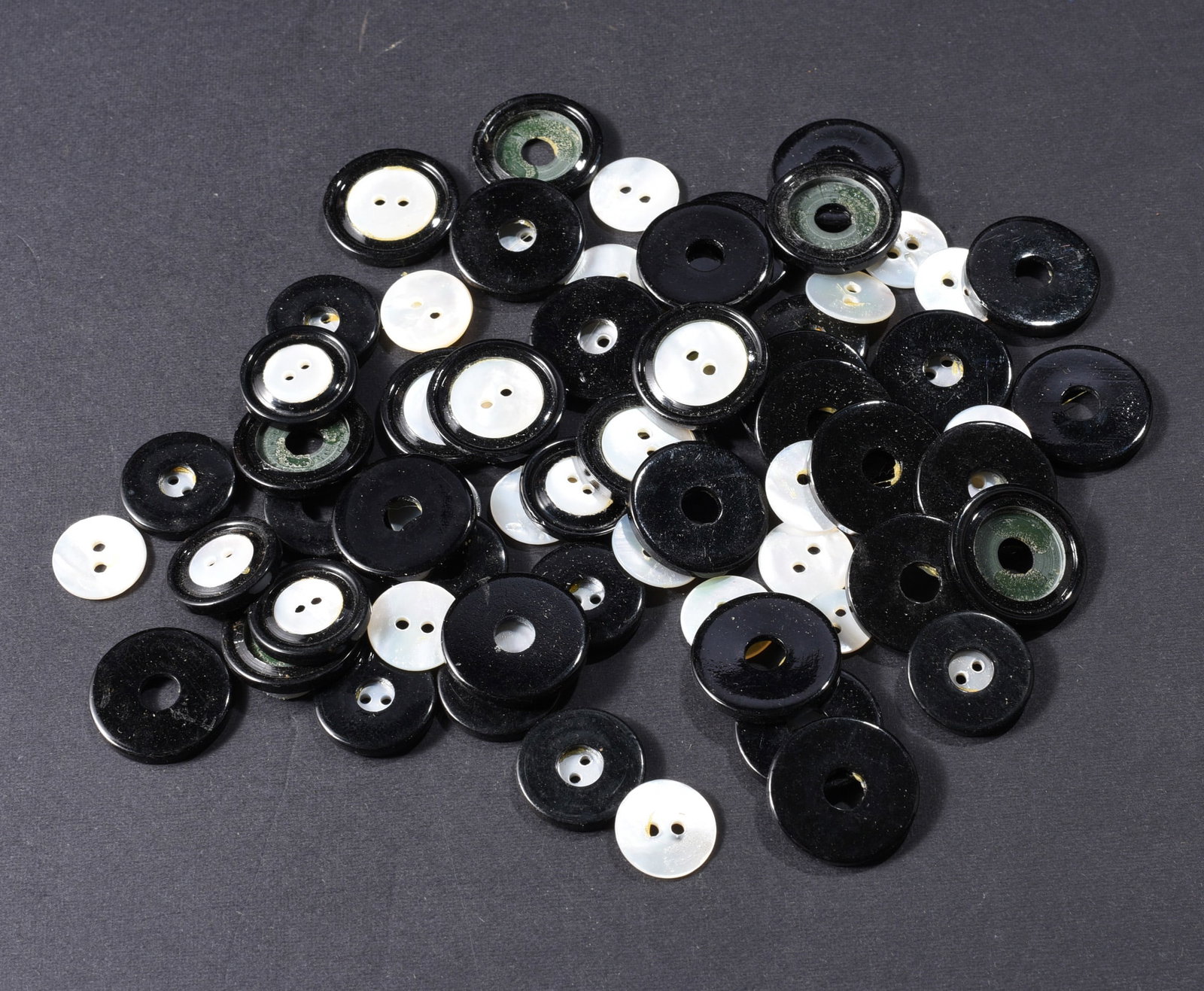 Collection of Black & Mother-of-Pearl Inset Buttons: Collection of black circular buttons and separate white mother-of-pearl or shell centers, including numerous assembled two-tone examples. The finished buttons feature luminous white shell disks set wi