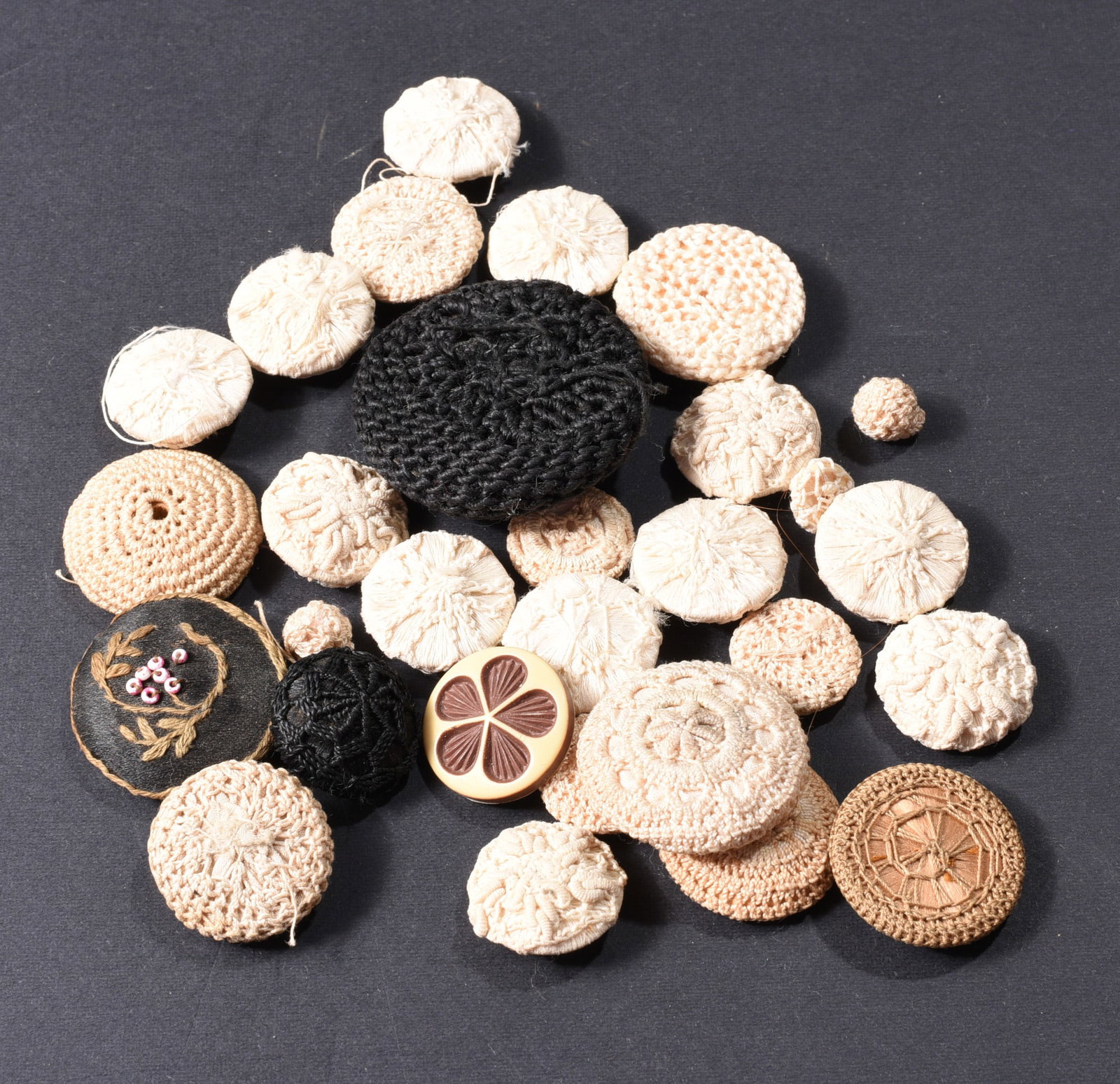 Collection of Vintage Crocheted & Fabric-Covered Buttons: Collection of approximately thirty vintage textile-covered buttons in cream, beige and black. Includes crocheted, woven, embroidered and thread-wrapped examples in numerous sizes, highlighted by sever