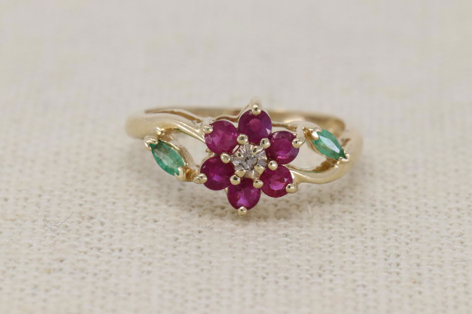 14Kt Ladies Diamond, Ruby's and Emerald Ring: A Ladies 14kt Yellow Gold Diamond ring. The ring has a round diamond in the center and 6 round Ruby's set around the center diamond and 2 Marquise Cut Emerald Stone on the sides. Ring size: 6.00. Tota